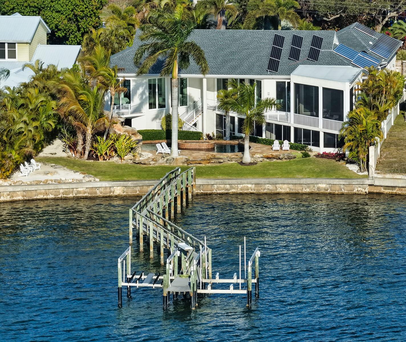 Big bay views surround you from this exquisitely updated waterfront estate. Welcome to 324 Bayshore Drive, a property of nearly half an acre set on a large, open stretch of the bay with easy access to the Intracoastal Waterway. Even more spectacular is the beautiful water and natural beauty of Midnight Pass which is just to the north of this property and sandbar relaxation just a short boat ride away. This home features all the right spaces and updates- it features a smartly renovated main house comprised of three bedrooms, three and a half bathrooms and spacious office, as well as separate guest suite with full bathroom. From the moment you approach this property you can tell something is different about it. The large front yard features a wraparound drive with tasteful landscaping and as you approach the front door you are transported into true relaxation as you enter over a pool with footbridge to the front door. The immediate thing you will notice are unobstructed beautiful views, high ceilings and stunning architecture.  As you take in the 36x36 tile updated flooring you’ll visit the kitchen and great room.  The kitchen features upscale appliances from SubZero, Miele and Thermador, as well as sleek European style cabinetry. The main living space opens onto a screened, elevated patio with built-in summer kitchen.  The primary is oversized with soaring ceilings and features a spa-like bathroom with free-standing tub, walk-in shower, dual vanities, and walk-in closet. The real fun begins outside- it’s hard to beat the outdoor living space- private sandy beach, heated pool and spa, and large fenced backyard to enjoy.  The boating enthusiast will enjoy dual 16k and 10k boat lifts, fish cleaning station, water and electrical service. This home features its own video security system, solar panels with battery backup, a full complement of hurricane shutters, and is located in flood X, indicating no flood insurance required. The roof was replaced in 2025,  the structure is built strong with ICF concrete block construction, and the attic  insulation is spray foam for energy efficiency.  This special estate must truly be seen in person to grasp- schedule your private showing today.