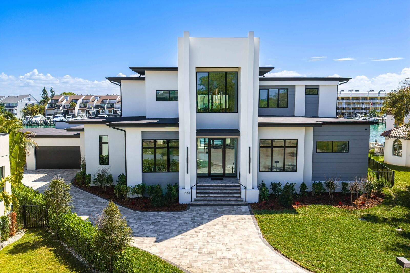 Defined by a rarely found 155 +/- feet of seawall and deep-water dockage with accommodations for large vessels or multiple watercraft, this visually stunning new construction estate is positioned among a collection of newly constructed waterfront homes. Capture the advantage of newer luxury construction paired with a sought-after boating and waterfront lifestyle in Tierra Verde. Built to elevated standards, this commanding and impressive residence pairs timeless elegance with modern coastal design. A grand foyer with soaring ceilings welcomes you into a light-filled living room with statement lighting and expansive sliding glass doors, all framing sweeping water views. An open chef’s kitchen provides for decadent entertaining with dual islands, quartz waterfall countertops, top-of-the-line Wolf and Sub-Zero appliances, a full-size Sub-Zero beverage refrigerator, along with a butler’s pantry, and an additional walk-in pantry. The first-floor primary suite delivers a private waterfront retreat with serene water views, automated shades, dual custom walk-in closets, a laundry area, and an opulent spa-inspired bath with floating dual vanities and a marble wet room with soaking tub. Additional first-floor spaces include a breakfast area with panoramic water views, office, powder bath, laundry room, and mudroom. Transition to the second level via a private elevator or the dramatic staircase to an open lounge with an entertaining wet bar and a covered terrace through expansive sliding glass doors, with water views beyond. The second level also hosts three spacious ensuite guest rooms. Enjoy seamless resort-style indoor-outdoor living with spectacular water views, a saltwater pool and floating spa, composite dock, and 20,000-pound boat lift with boating access to Pass-a-Grille Channel and the Gulf. Additional appointments include a dog-wash station in the expanded laundry room, 24 kW generator, tankless water heater, water purification system, and 3-car garage. Expansive terraces, numerous covered entertaining areas, and beautifully manicured grounds complete the outdoor living experience. Discover the ultimate yachting lifestyle in Tierra Verde’s island enclave celebrated for its deep-water canals, island estates, and unobstructed Gulf access with no fixed bridges. Step from your backyard onto the water and cruise to Shell Key, Egmont Key, and the pristine beaches of Pass-a-Grille. Near numerous waterfront restaurants and luxury resorts, this exceptional location provides an unparalleled combination of private island serenity, premier boating and one of Tampa Bay’s most coveted coastal lifestyles.