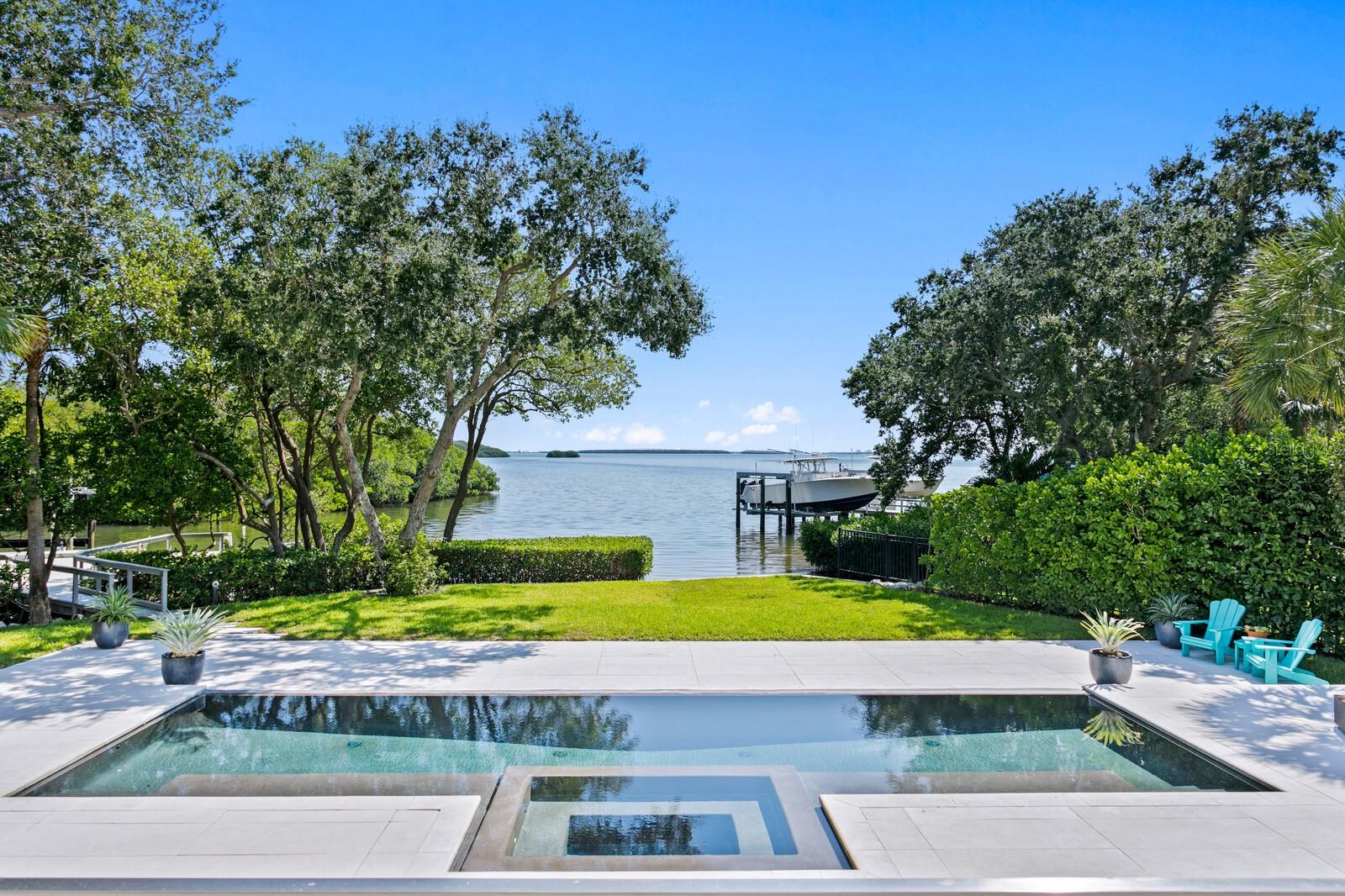 Experience the ultimate in luxury and privacy at this breathtaking contemporary waterfront estate, boasting over 143’ of pristine water frontage. High and dry elevated construction with current flood insurance policy only $671/yr ! Situated on a rarely found .77 acres of meticulously landscaped, park-like grounds, this Tierra Verde estate offers an unrivaled coastal lifestyle. This rare slice of paradise includes over 4,400 sq. ft. of sophisticated modern living, breathtaking water views, and a private deep-water dock with a 20,000 lb. boat lift. Upon arrival, you are greeted by a long circular driveway shaded by a canopy of manicured trees. Step through the grand foyer to a sleek, light-filled interior, where a floating staircase and soaring ceilings create an awe-inspiring entrance. Floor-to-ceiling windows capture panoramic water views, while a gas fireplace adds warmth to the expansive living area. The gourmet kitchen is a chef’s dream, featuring top-of-the-line appliances, European cabinetry, an induction range, and a glass-enclosed wine cellar — all perfectly designed for entertaining. An office/optional bedroom with ensuite full bathroom completes the first-floor spaces. Ascend the magnificent floating staircase and retreat to the opulent primary suite with its own private waterfront terrace, a spa-like bathroom with a zero-entry shower, soaking tub, and custom closets. Three additional ensuite bedrooms provide ample space for family and guests. Designed for seamless indoor-outdoor resort style living, the lushly landscaped backyard is a private sanctuary complete with an oversized heated infinity pool, spa, fire pit, and an oversized terrace for entertaining. Additional features include hurricane impact windows and doors, a low-cost assumable flood insurance policy, newer metal roof, a whole-home water filtration system, automatic shades, surround sound speakers, a newer seawall. and 3 car garage. Just minutes from award-winning beaches, downtown St. Petersburg, and only 30 minutes from Tampa International Airport, this waterfront estate is the epitome of coastal luxury and privacy.