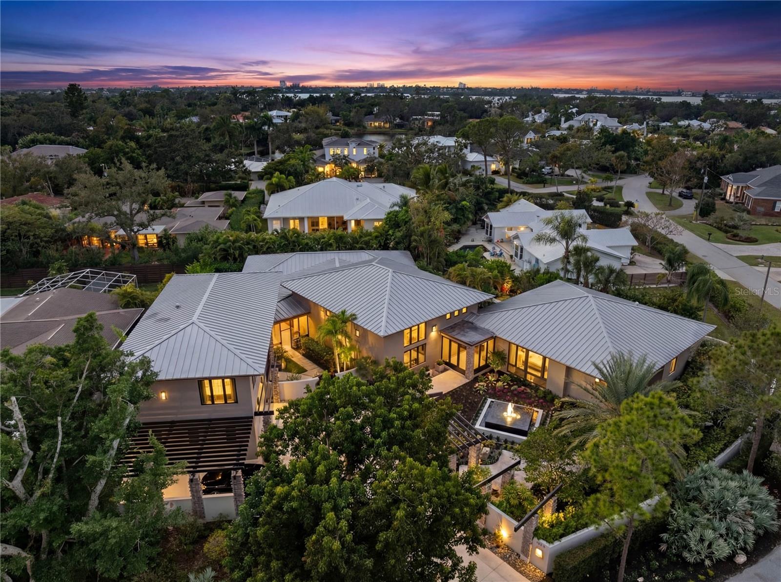 A residence of sophistication and luxury, this exceptional home was thoughtfully designed to bring family and friends together—sharing good food, meaningful connection, and the enjoyment of elevated everyday living. Ideally located just 8 miles from Sarasota-Bradenton International Airport, 12 minutes to Siesta Key Beach, and 10 minutes to downtown Sarasota, the property is in close proximity to The Ringling, Van Wezel, Selby Gardens, Asolo, premier dining and shopping, The Field Club, and the Sarasota Yacht Club—creating a seamless blend of culture, convenience, and coastal lifestyle. Elegant yet warm and approachable, the home blends refined architecture with tropical elements, including stone columns, metal pergolas, concrete textures, and lush landscaping, creating a relaxed oasis unlike any other. A surrounding stucco wall enhances privacy, allowing you to unwind to the soothing sound of a tranquil fountain within a peaceful, secluded setting. The main living spaces were intentionally designed for gathering, featuring bead-board stained ceilings in the family room, formal living room, and dining area. The cook’s kitchen is both striking and highly functional, highlighted by a glazed pressed-tin ceiling, unpolished concrete floors, and views into the kitchen garden through multiple French doors and expansive windows—perfectly suited for both everyday living and entertaining.