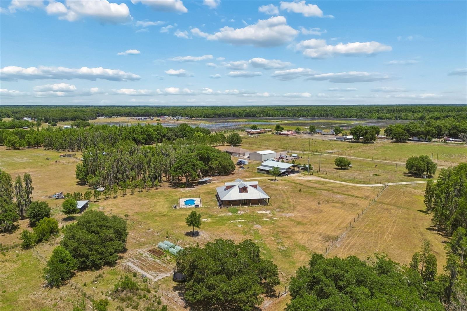 Welcome to your private, thoughtfully engineered farmhouse retreat on 10 fully fenced acres—designed for both beauty and resilience. Built on an elevated concrete slab foundation with reinforced rebar tying into block construction and Hardie board exterior, this home has experienced zero water intrusion through recent hurricane seasons, offering true peace of mind.

A charming concrete wraparound porch with pebble epoxy flooring, tongue-and-groove pine ceilings, recessed lighting, and high-powered fans creates the perfect outdoor living space. Inside, the open-concept floor plan features 3 bedrooms and 2 baths, with luxury vinyl flooring throughout and abundant natural light from large hurricane-impact windows. 

The gourmet kitchen is a showstopper with hardwood maple cabinetry, hidden storage, Rev-A-Shelf upgrades, walk-in pantry with automatic lighting, and a full suite of stainless steel appliances including a gas cooktop and wall oven/microwave combo. A stone-accented gas cooking area and gas fireplace add warmth and character to the living space.

The primary suite offers a walk-in shower, spacious walk-in closet with a secure safe pocket, and custom finishes throughout. Additional upgrades include spray foam insulation, tankless gas water heater, water softening system with reverse osmosis, new adjustable blinds, and a whole-home wiring setup for a PTO/tractor generator system.

Step outside to your wrap around porch or fenced, heated pool and spa with automated cleaner, plus a screened outdoor kitchen and fish cleaning station. The property is fully equipped for rural living with a 64x40 barn (partially built out with water and electric), chicken coop, 4-bay dog kennel, raised irrigated garden beds, and multiple fruit trees.

Bring your horses, cattle, RV, and all your toys—this property is fully cattle fenced, includes an RV hookup, underground 500-gallon gas tank, irrigation around the home and pool, and a commercial-grade seamless metal roof with full hurricane strapping.

This one-of-a-kind property combines high-end finishes, smart construction, and functional land use—perfect for those seeking a self-sufficient lifestyle without sacrificing modern comfort.