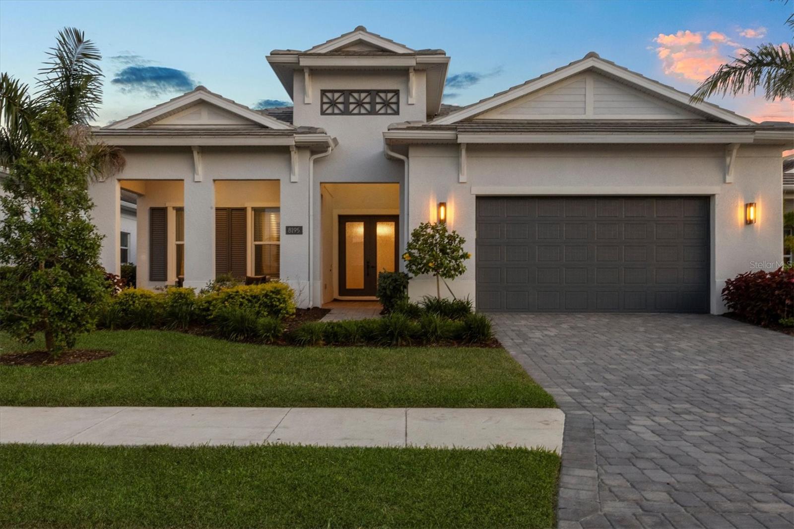 Enter into refined luxury in The Isles at Lakewood Ranch, where this impeccably appointed three-bedroom, four-bath residence offers an unparalleled blend of elegance and functionality. A paver driveway leads you past lush, meticulously landscaped grounds to a welcoming front porch with seating, framed by double-glass entry doors that set the tone for the exquisite craftsmanship found throughout. Upon entry, soaring ceilings and designer lighting illuminate wood-style tile flooring beneath your feet that spans throughout. The foyer—adorned with custom shiplap walls—flows seamlessly from a built-in garage drop zone into an expansive, open-plan living area. Here, intricate beam and ceiling details crown the space, while expansive sliders open to the lanai, blurring the line between indoor and outdoor living. An adjacent dining area provides an intimate setting for gatherings. At heart of the home, the chef’s kitchen is a study in sophistication with KitchenAid appliances, including a double oven and gas cooktop, beautifully contrasted by quartz countertops and floor-to-ceiling cabinetry. A generous center island, ideal for meal preparation and casual entertaining, anchors the room. The sumptuous primary suite offers a serene retreat, complete with a deep soaker tub, quartz countertops at the long double vanity, marble-inspired tile flooring, a glass-encased shower and a sprawling custom walk-in closet. Two guest suites, each featuring walk-in closets and en-suite baths, provide privacy and comfort. A versatile flex space, also equipped with an en-suite bath and pool access, invites use as a den, bonus room or additional guest quarters. Outside your screened lanai, entertain effortlessly in the outdoor kitchen or unwind by the heated saltwater pool and spa, complete with sun shelf and cascading waterfall. Additional quality features include a whole-home water filtration system, integrated security and impact-resistant glass, ensuring comfort and uncompromising peace of mind. Beyond your doorstep, The Isles at Lakewood Ranch delivers a lifestyle of leisure and wellness. This prestigious, gated community features a beautifully appointed clubhouse with social gathering spaces, a resort-style pool, state-of-the-art fitness center, and lighted tennis and pickleball courts. Miles of scenic recreational and biking trails meander through lakeside parks and playgrounds, while year-round community events foster neighborly camaraderie. Experience luxury living at its finest in The Isles at Lakewood Ranch.
