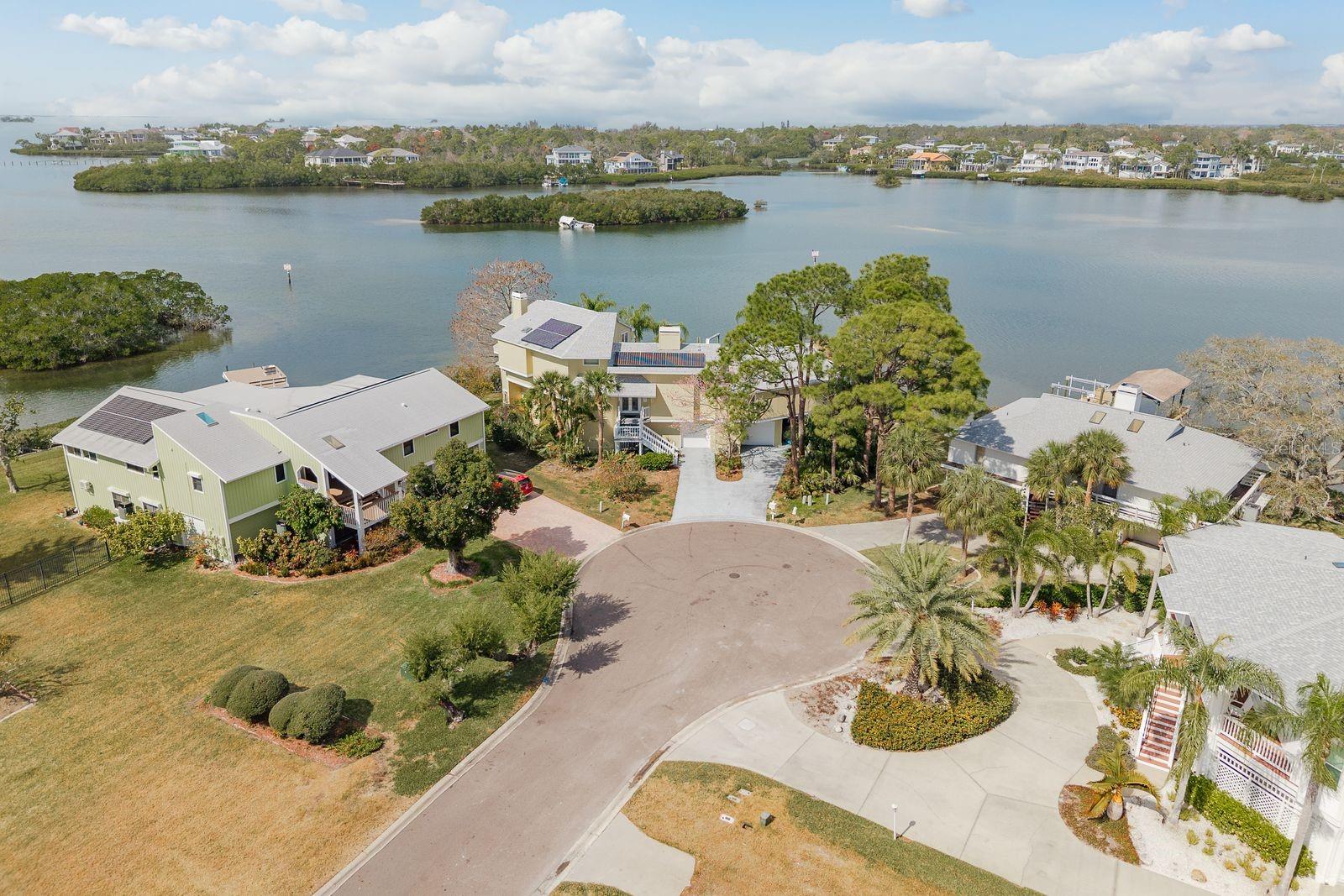 MAJOR PRICE ADJUSTMENT! Welcome to the ultimate boatable waterfront retreat offering unparalleled views of Southerland Bayou at the entrance to the Intracoastal Waterway. Perfectly positioned in the highly sought-after Ozona community on a quiet cul-de-sac, this waterfront residence offers breathtaking panoramic water vistas from every room along with rare deep water access and direct access to the Intracoastal Waterway and Gulf, making it a true boater’s paradise. The charming keywest façade, eco-friendly solar power, expansive living spaces, and incredible bones create a rare opportunity for a buyer to bring their vision and decorator’s touch to transform this property into a spectacular custom waterfront estate. From the main level, endless water views immediately captivate throughout the open-concept design featuring soaring ceilings, a cozy wood-burning fireplace & a wraparound covered porch showcasing stunning 180-degree water views. Below, enjoy a sparkling pool & lanai, private dock, and covered boat lift. The spacious entertaining areas include a large bar area flowing into the oversized kitchen complete with granite countertops, stainless steel appliances, custom wood cabinetry & a breakfast bar overlooking the water. Adjacent is a formal dining room with intricate ceiling detailing & sweeping water vistas. An additional office/bedroom/in-law suite offers built-in bookshelves & an attached half bath with potential to convert to a full bath, while a closet pantry, separate laundry room & electric dumbwaiter add convenience and functionality. On the opposite wing, two generously sized guest bedrooms offer sliding door access to the lanai & share a Jack-and-Jill bathroom with dual vanities and granite countertops, along with an additional guest bath and spacious office/5th bedroom with another bathroom. Up the grand open staircase, discover the luxurious primary retreat featuring soaring wood ceilings, a versatile bonus room ideal for an office, nursery, or additional closet, a hobby room or oversized walk-in closet & a beautifully appointed en-suite bath with an oversized soaking tub, seamless glass walk-in shower, double vanities, private water closet, and custom walk-in closet with built-in organization. A charming sitting room with a gas fireplace and vaulted ceilings adds warmth and character while plantation shutters and a private covered balcony provide the perfect place to take in the spectacular coastal views and breezes. The ground level offers excellent potential for an in-law suite with a full pool-access bathroom, living room, kitchenette with granite counters, and an additional enclosed flex room recently refurbished, ideal for guests or multi-generational living. Two spacious garages, a workshop, and abundant storage complete the space. While the home could benefit from cosmetic updates and modernization, the possibilities are endless for creating a stunning luxury waterfront showcase. Notable upgrades include three HVAC systems (2017, 2018, 2020), Roof 2018, monitored alarm system, two boat docks, and solar power. Situated in a beautifully maintained HOA-free upscale neighborhood just minutes from downtown Palm Harbor and Crystal Beach, with endless dining, shopping, award-winning beaches, excellent medical facilities, top-rated schools, and Tampa International Airport only 30 minutes away, this rare waterfront gem offers luxury living, privacy, unmatched boating access, and the ultimate Florida coastal lifestyle.