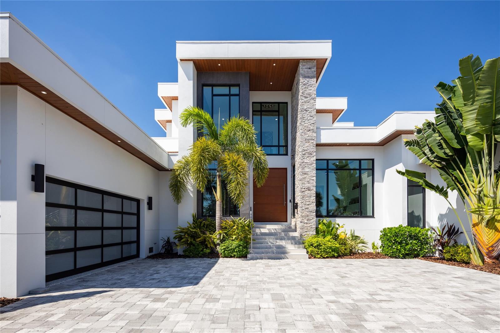 Introducing a Contemporary Waterfront Masterpiece in Tampa Bay. Striking modern architecture and clean, minimalist design come together in this extraordinary custom-built waterfront residence. Completed in 2023, this home makes a bold statement with its commanding curb appeal, soaring 28-foot entry, and dramatic 23-foot foyer. Brilliant natural light, soaring ceilings, and meticulous craftsmanship set the stage for a refined coastal lifestyle.
The open-concept floor plan highlights a chef’s dream kitchen with custom cabinetry, pearl-white quartz island, Thermador appliances, gas cooking, full-height wine chiller, and built-in espresso machine, complemented by a discreet butler’s pantry. Expansive living and dining areas open seamlessly to the water, while the executive-style office and designer guest bath add both elegance and function.
The owner’s suite is a private sanctuary with breathtaking views, balcony access, dual walk-in closets, and a spa-inspired bath featuring custom vanities, a Jacuzzi soaking tub, and a glass-enclosed multi-head rain shower. Upstairs, two additional en suite bedrooms and a large media room extend to a 330-square-foot covered terrace with commanding views of the bay.
Outdoor living is elevated with over 1,200 square feet of covered waterfront terraces, a resort-style pool and spa, outdoor kitchen, and lush landscaping. Waterfront amenities include an updated seawall, large composite dock, kayak/paddleboard launch, boat lift, and mooring capacity for a sizable yacht.
Located just ten minutes from downtown St. Petersburg and six minutes from the Gulf beaches, this residence offers an extraordinary blend of serenity and convenience. Nestled within the highly coveted, gated enclave of Bayway Isles, the community is distinguished by its 24/7 guarded security, pristine surroundings, and enduring sense of privacy.
This estate is not simply a residence but a testament to vision, artistry, and uncompromising craftsmanship. More than a home—it’s a statement of modern luxury and life without compromise. Arrange your private showing today and experience the pinnacle of waterfront living.