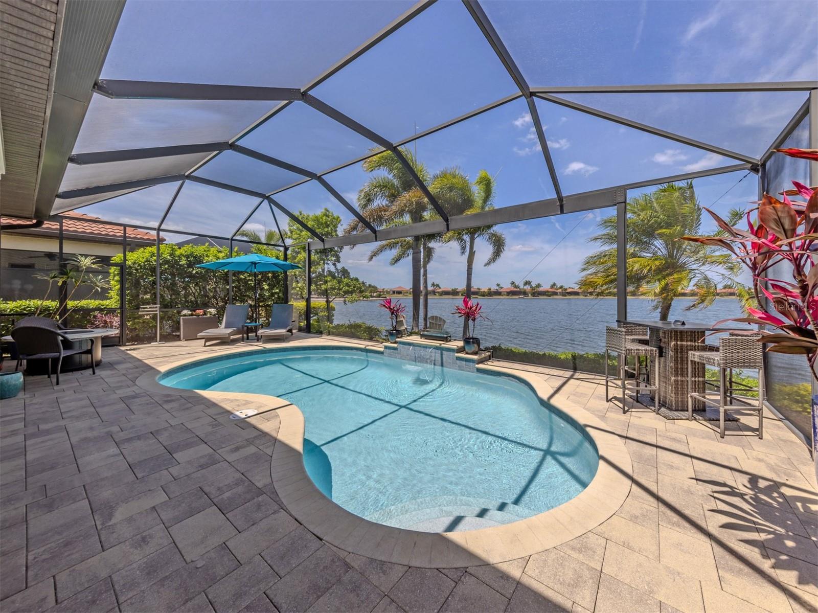 Experience the ultimate Florida lifestyle in this exquisite lakefront residence in Toscana Isles, one of the area’s premier resort-style communities. Perfectly positioned on a beautiful lake, this exceptional home offers breathtaking water views and stunning sunsets. For seamless indoor-outdoor living, sliding glass doors open from the great room to the expansive lanai, providing effortless flow for entertaining and everyday living. Thoughtfully designed to expand the living area, the lanai showcases unobstructed views through clear-view screens, a saltwater pool with new LED lighting for evening ambiance, and a complete custom outdoor kitchen. Inside, the interior presents a modern coastal, open-concept great room designed to maximize light and views while the tray ceiling with a large contemporary ceiling fan adds architectural depth. Gourmet kitchen boasts white cabinetry, Cambria quartz countertops, pendant lighting and a large center island that doubles as a breakfast, creating a polished yet relaxed gathering space. Primary suite is a serene retreat overlooking the lake with tray ceiling, crown molding, a walk-in closet plus a secondary closet and an automatic motorized window shade for light control. Spa-like en suite bath has a garden tub, walk-in shower and dual sinks with a vanity area. Two additional bedrooms, another full bath, versatile den, laundry room, and two-car garage complete the home. In addition, an electric roll-down hurricane screen on the lanai, along with a portable generator hookup, offers added peace of mind during storm season. Toscana Isles delivers true resort-style living. Enjoy over 200 acres of lakes perfect for kayaking, paddleboarding, fishing, and more. The Tuscan-inspired clubhouse features an infinity pool, fitness center, billiards, bar, and event spaces. Outdoors, residents love tennis, bocce, a dog park, and one of the area’s most active pickleball programs. All this is just two miles from Sarasota Memorial Hospital, six miles from Nokomis Beach, and minutes to Venice Island’s shops, dining, and world-class Gulf sunsets.