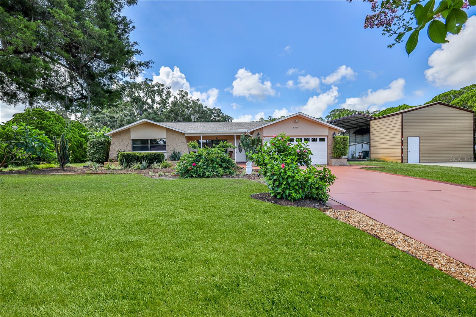 Bring your RV, boat, and all your toys! Nestled on 1.87 beautifully landscaped acres with scenic lake views, this one-of-a-kind property offers the privacy, space, and natural beauty that's becoming increasingly difficult to find. Surrounded by lush tropical gardens and mature landscaping, the grounds feature live oaks, hibiscus, gardenias, azaleas, banana grove, loquat, orange and grapefruit trees, mulberries, an established tomato garden, and a spectacular 18-foot poinsettia, creating a truly tranquil park-like setting.
Inside, this well-maintained, 4-bedroom, 2.5-bath home offers a spacious (1,988sq ft heated) and functional layout with a welcoming living room, family room, dining area, and an open kitchen featuring stainless steel appliances, coffee bar, pantry, and abundant cabinetry. The primary suite includes a large walk-in closet, ceiling fan and updated bath with granite countertops, beautiful tile work, and a step-in shower. Three additional bedrooms provide comfortable accommodations with luxury vinyl plank flooring, ceiling fans and generous closet space. Enjoy Florida living year-round from the screened lanai overlooking the peaceful surroundings. The property is designed for both recreation and practicality, featuring an attached 2-car garage, RV pole barn, additional parking pad, 12' x 20' metal storage building with roll-up door, well house with electricity, generator hookup runs the well and refrigerator, mosquito treatment June 2026 and abundant storage throughout. Major updates include a 2023 Roof, 2022 HVAC system, new 200-amp electrical panel, impact-resistant sliding glass door, storm-rated shower window, whole-house water treatment system, water softener, well bladder (2024), and well pump (2026). A sprinkler system helps maintain the lush grounds year-round.
Bordered by a picturesque cypress swamp and seasonal stream, this property offers a rare blend of privacy, natural beauty, and convenience. If you're searching for acreage, room for your RV and boat, no HOA restrictions, and a peaceful Old Florida lifestyle, this exceptional property is a must-see.