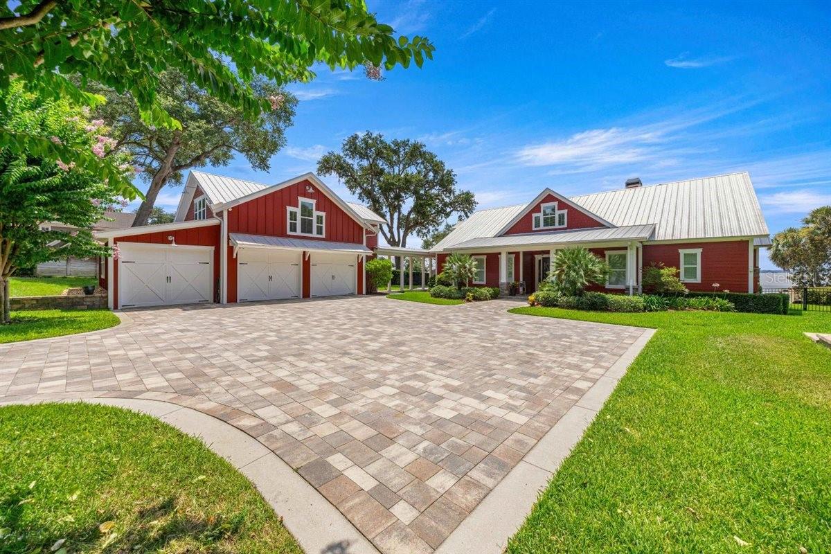 Welcome to this custom waterfront estate where every detail has been meticulously crafted for maximum enjoyment! Sitting on a prime 2-acre parcel on beautiful Lake Weir—a premier destination for boaters, skiers, and water enthusiasts—this direct lakefront property is a true showstopper. Approached by a tree-lined drive, the residence was built in 2017 with durable HardiePlank siding and metal roofing, and features a striking red color scheme with bright white trim. The main home offers 3,619 heated square feet (5,934 total square feet under roof) configured with 4 bedrooms, 4 full en-suite bathrooms and 2 half baths. Inside, the layout is defined by varied architectural transitions and high ceilings throughout, featuring custom tray, coffered, and cathedral designs. The lake-facing side is lined with large windows, offering expansive, unobstructed views. The master suite is oversized and has direct access to the porch and pool areas off the back of the home, plus a glamour bath and huge closets with storage systems. One of the guest bedrooms has built-in bunking with multiple beds for maximum use of the square footage, with both also having en-suite bathrooms. The kitchen is equipped with custom cabinetry, premium stainless-steel appliances, a professional-grade range, an inset refrigerator, and a built-in under-island appliance station. Immediately adjacent, a functional secondary pass-through staging area supplies extra cabinetry and supplemental appliances for seamless hosting. A separate dining area and a home office complete the main floor's footprint. Upstairs, the home expands into a large open bonus area, a designated hobby/game room, and an oversized, climate-controlled storage room. There are also multiple storage closets throughout the home plus a dedicated tech closet to hold security systems, surround sound equipment, etc.
Perfectly separating guest or multi-generational living, a self-contained auxiliary suite sits independently above the attached 3-car garage, complete with a spacious open floor plan, a fully equipped kitchenette, and a private full bathroom. The estate's mechanical footprint features dual high-efficiency HVAC systems, professional exterior landscape uplighting, and integrated surround sound speakers wired both inside and out. The power infrastructure is anchored by a whole-house standby generator tied to an on-site liquid propane (LP) gas tank, which also services the kitchen range, interior fireplace, pool heater, and outdoor fire pit. The outdoor living spaces are designed for ultimate lakeside entertainment, centered around a screen-enclosed in-ground pool and integrated hot tub, a dedicated grilling station, covered brick-paver patios, structural pergolas, and an outdoor shower. Engineered terracing and structural retaining walls lead down to approximately 100 linear feet of white sand beach frontage. From the shoreline, a long-plank walkway extends to a covered boathouse equipped with a motorized boat lift and dedicated side-tie mooring for secondary boats and jet skis, terminating at a thatched tiki cabana plumbed with power and water. Completing this exceptional acreage is a separate 40×52 foot structural metal building at the top of the property, engineered with three standard bay doors, one high-clearance RV overhead door, and an attached side carport for secure storage of boats, trailers, and recreational equipment. This home offers the ultimate lakefront living experience and is a must-see!