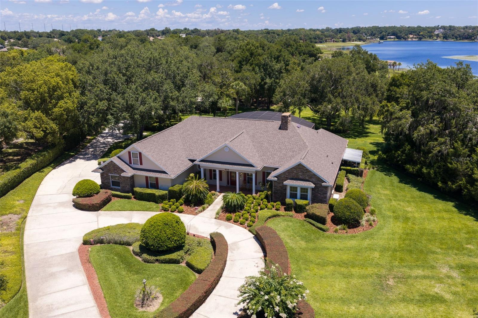 Welcome to a private estate where luxury, recreation, and exceptional craftsmanship come together to create an unparalleled Florida lifestyle. Nestled on approximately three beautifully landscaped acres in Eustis, just minutes from charming downtown Mount Dora, this one-of-a-kind property offers over 3,825 square feet of elegant living space designed for both grand entertaining and everyday comfort.
From the moment you arrive, the circular driveway, mature landscaping, and impressive estate presence set the tone for what awaits inside. Soaring ceilings, refined architectural details, spacious gathering areas, a dedicated home office, and a private theater room create a home that is both elegant and inviting. Pocket sliding doors seamlessly connect the interior living spaces to an extraordinary outdoor retreat. The resort-style saltwater pool and spa feature a beach entry, cascading waterfalls, tropical landscaping, expansive stone decking, and picturesque lake views, all enclosed within a spectacular screened lanai. Multiple covered entertaining areas, ceiling fans, outdoor dining spaces, and comfortable gathering areas create the feeling of a private Florida resort designed for year-round enjoyment. The spacious owner's retreat offers direct access to the lanai, dual walk-in closets, and a spa-inspired bath, while guest accommodations are thoughtfully positioned to provide comfort and privacy. One of the property's most remarkable features is the impressive detached RV, boat, and recreational garage. Designed for enthusiasts who need space to store, maintain, and showcase their collection, this extraordinary structure offers approximately 2,940 square feet of highly versatile space with insulated construction, soaring ceilings, oversized garage doors, extensive storage, workshop areas, and commercial-style 72-inch ceiling fans. Whether accommodating RVs, boats, classic cars, recreational vehicles, motorcycles, or hobby equipment, this exceptional building provides a level of flexibility and functionality rarely found in residential properties. Recent improvements include a new roof, updated HVAC systems, new kitchen appliances, a new pool and spa heater, updated wood flooring, refreshed exterior finishes, and numerous additional enhancements that reflect the pride of ownership found throughout the property. Additional features include a whole-house and pool generator system, hurricane shutters, an oversized attached garage, comprehensive surveillance system, mature landscaping, and scenic lake views that enhance the estate's peaceful and private setting. Whether you're searching for a luxury family retreat, an entertainer's dream, or a property that accommodates your passion for vehicles, boating, RV travel, and outdoor living, this exceptional estate delivers a lifestyle that is increasingly difficult to find. Conveniently located near downtown Mount Dora, Eustis, shopping, dining, golf, and the Harris Chain of Lakes, this is Florida estate living at its finest.