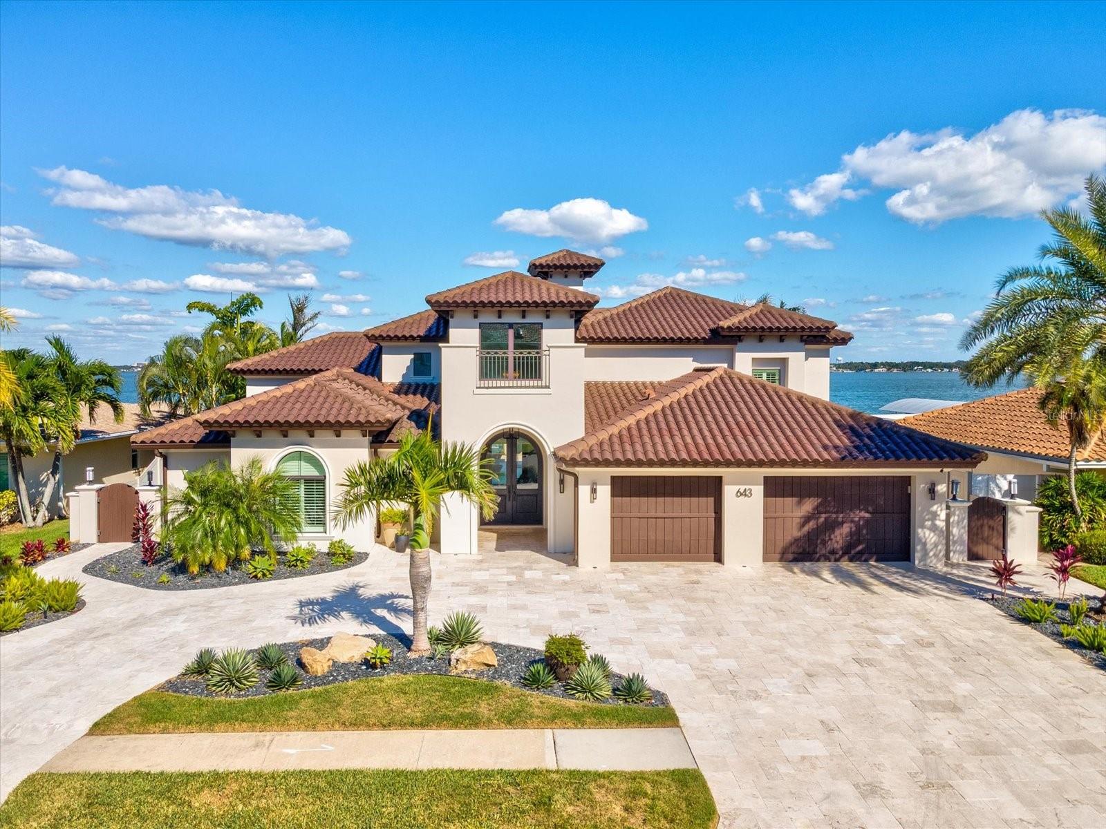 Experience unparalleled coastal luxury in this stunning Island Estates residence perfectly positioned on a ¼-acre lot with 180° unobstructed open-water views. This exquisite home offers 4 bedrooms plus an office, 3.5 baths, and a 3-car garage, seamlessly blending elegant design with state-of-the-art functionality. Boaters will delight in the deep-water dock featuring two lifts (including a 16,000 lb lift), shore power for larger vessels, and easy Gulf access for endless days on the water. The outdoor oasis is a true showpiece—complete with a heated saltwater pool and spa, waterfalls, fire bowls, and custom lighting, all framed by tranquil water views. Enjoy sunset cocktails or waterside dining beneath the charming gazebo, surrounded by lush tropical landscaping and added protection from the riprap seawall. Step inside through custom double doors to discover sophisticated living spaces, including a formal sitting room with a grand gas fireplace and sweeping views through custom French doors. The chef’s kitchen is equipped with high-end stainless steel appliances, a gas range, and overlooks the spacious living area with dual 4-panel sliders that open wide for seamless indoor/outdoor living. The owner’s retreat is a private sanctuary on the main level, featuring double-door entry, a Venetian-inspired en-suite bath with soaking tub, walk-in shower, and his-and-hers closets. Step directly outside to enjoy morning coffee by the pool as the sun rises over the water. Additional highlights include a temperature-controlled 800-bottle wine cellar, impact glass throughout, natural gas service for energy efficiency, and ample storage—including a walk-in attic and home automation system to control lighting, blinds, A/C, garage doors, surround sound, security cameras, and more. Upstairs are three guest suites, each with dedicated bath access, and an office (or fifth bedroom) with private balcony, dedicated ventilation, and air purification system—ideal as a cigar room or quiet retreat. Located on Island Estates’ most desirable street, this property benefits from sidewalks, underground utilities, and a higher elevation. Enjoy the convenience of this golf cart-friendly community featuring its own grocery, shops, and dining—all just moments from Clearwater Beach and Clearwater Sound’s live entertainment. This exceptional home captures the very best of luxury waterfront living—sophisticated, smart, and perfectly situated for the ultimate Florida lifestyle.