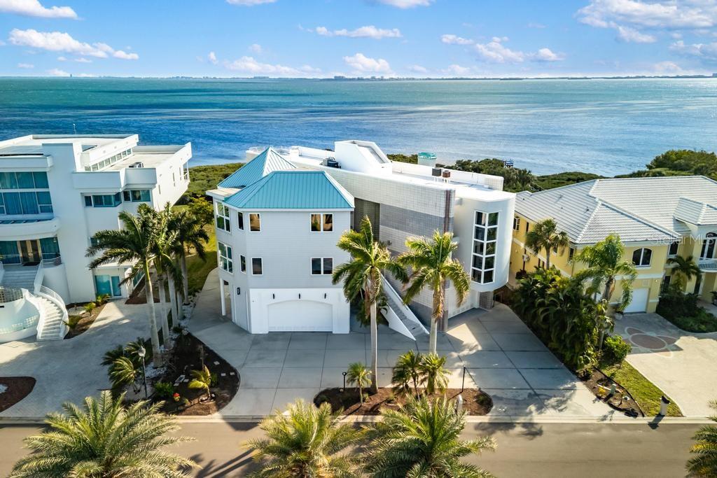 One or more photo(s) has been virtually staged. A truly one-of-a-kind Sarasota Bay waterfront estate set within the private gated enclave of Esplanade on the Bay, offering rare scale, architectural distinction, and 100 feet of direct Sarasota Bay frontage. Encompassing 7,862 square feet under air and 12,088 total square feet, the residence showcases a striking architectural presence shaped by its waterfront setting.

Originally featured in a regional architectural publication for its innovative “Tri-Plexity” concept—uniting three distinct architectural ideas into one cohesive waterfront composition—the home reflects a forward-thinking approach to form, vertical volume, and the intentional framing of Sarasota Bay from nearly every room.

Upon entering the main living level, sweeping views of Sarasota Bay unfold through expansive walls of glass as the living room rises to 18-foot ceilings and features a fireplace, while floor-to-ceiling windows frame the water and fill the interior with natural light, creating a dramatic yet welcoming atmosphere.

From the living room, the home unfolds into surrounding living spaces with the gourmet kitchen positioned at the center of the layout. It features a large center island, professional gas cooktop, premium appliances, and extensive cabinetry arranged to connect seamlessly with the surrounding areas while maintaining views toward Sarasota Bay. Adjacent to the kitchen, a light-filled casual dining space overlooks the bay and opens to a private balcony, creating a beautiful setting for morning coffee or relaxed meals.

Beyond the kitchen, a formal dining room provides an elegant setting for gatherings and special occasions and opens to a spacious balcony overlooking Sarasota Bay, complete with a spiral staircase leading to the ground level. Just past the dining room, a seating area with views of Sarasota Bay offers a relaxed place to enjoy the waterfront setting while remaining connected to the surrounding living spaces.

This level also includes a private study, a full bathroom, and an additional bedroom. A guest bedroom is positioned in its own wing near the laundry and features a private full bathroom, sitting area, and a separate exterior entrance, creating a private and welcoming guest suite for visitors.

The upper level features the expansive primary suite with fireplace and private balcony overlooking Sarasota Bay, ideal for enjoying tranquil water views and spectacular sunsets. Also located on this level are two additional bedrooms, each with its own en-suite bathroom, along with a spacious media room with its own bathroom. A private elevator connects the ground, main living, and primary suite levels.

The ground level includes a large fitness area, lounge space, and bathroom, along with two attached garages accommodating up to seven vehicles.

Outdoor living features a heated saltwater pool and spa within a screened terrace, designed for relaxation and entertaining, with space for outdoor dining and the potential for an outdoor kitchen.

A private dock extends from the property’s Sarasota Bay frontage, providing convenient access to the water for kayaking, paddleboarding, or simply enjoying the waterfront lifestyle.

Located minutes from IMG Academy, Sarasota-Bradenton International Airport, shopping, dining, and the beaches of Anna Maria Island and Longboat Key, this extraordinary residence stands as a distinctive architectural waterfront home along Sarasota Bay.