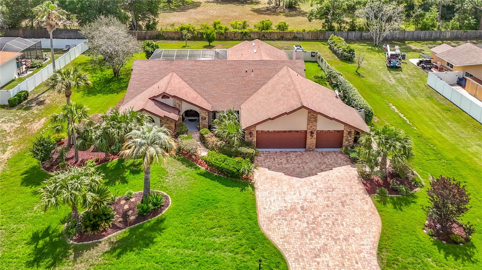 Welcome to one of Hernando County's most sought-after gated communities, where towering oak trees, estate-sized homesites, scenic lakes, and custom-built homes create an atmosphere of privacy, beauty, and distinction.  Situated on a beautifully landscaped homesite, this exceptional pool home offers the perfect blend of luxury, comfort, and Florida living.  From the moment you arrive, you'll be impressed by the lush tropical landscaping, expansive brick paver driveway, and oversized garage that create stunning curb appeal.  Inside, soaring ceilings and spacious living areas provide an open and inviting floor plan designed for both everyday living and entertaining. The updated kitchen features quality cabinetry, solid surface countertops, stainless steel appliances, abundant storage, and overlooks the main living areas, allowing family and guests to stay connected.  The impressive family room showcases a dramatic stone fireplace, abundant natural light, and seamless access to the outdoor living spaces. Beautiful ceramic and porcelain tile flooring flows throughout much of the home, creating a timeless and elegant feel.  Retreat to the spacious owner's suite featuring a beautifully updated spa-inspired bathroom complete with a large walk-in shower, soaking tub, and quality finishes throughout.  Step outside to your own private backyard oasis. The expansive screened lanai surrounds a sparkling pool and generous entertainment space, while the outdoor kitchen creates the perfect setting for family gatherings, weekend barbecues, and year-round Florida enjoyment.  The partially fenced yard is beautifully maintained and is perfect for privacy, or to use as a dog run so your pets are kept safe and secure when outdoors.  Beyond the property itself, Lake in the Woods offers an exceptional lifestyle rarely found in today's communities. Residents enjoy a secure gated entrance, a golf cart friendly neighborhood with scenic lakes, tennis courts, pickleball courts, playground areas, and a private community island that serves as a gathering place for neighborhood events, family activities, and social functions throughout the year. The mature landscape, winding roads, and natural beauty create a peaceful setting that feels worlds away while remaining just minutes from US 19, the Suncoast Parkway, shopping, dining, medical facilities, and the Gulf Coast.  This is more than a home—it's a lifestyle opportunity in one of Spring Hill's most desirable and established gated communities.