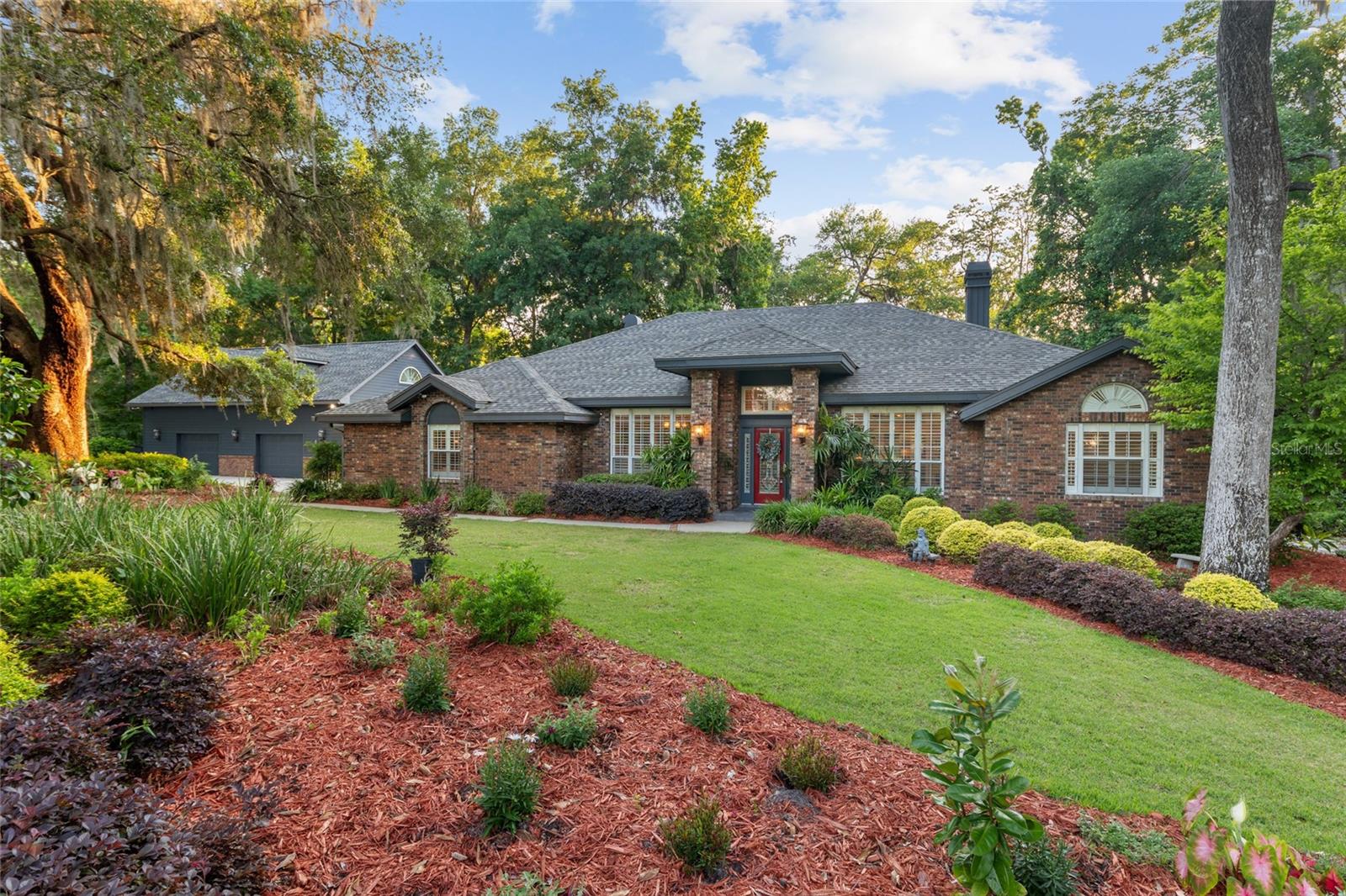 Welcome to RICHMOND. Framed by 1.46 acres of lush grounds and a striking brick construct, this single family residence offers a refined sense of arrival. A long, generous driveway winds through mature trees and curated landscaping, where privacy unfolds naturally. Centered around a scenic ravine and anchored by two majestic live oaks, the property was thoughtfully designed to embrace and highlight its natural surroundings. A spacious 2-bay, 1,300+ sq ft garage with room for up to four vehicles, paired with an accompanying apartment, adds both impressive presence and exceptional flexibility. Designed by Tom Hunt, the home reflects enduring craftsmanship paired with meaningful updates. Inside, polished engineered hardwood floors guide a natural flow through spaces that feel both open and intentional. Tall ceilings and crown moulding add architectural detail, while classic interior shutters carry throughout the home, softening light and creating cohesion. A welcoming front parlor opens into a main living area defined by vaulted ceilings and a brick fireplace, offering both scale and warmth. A flexible sitting room framed by glass paneled pocket doors offers an opportunity for a more private retreat or conversation space, with a full wall of windows drawing in natural light. The kitchen serves as a central gathering point, where cherry wood Busby cabinets, a 6 burner Thermador range, and expansive prep surfaces come together with ease. A nearby breakfast area flows into a Florida room style space, fully integrated and opening through French doors to the pool beyond. The primary suite is expansive, with its own fireplace and a private sitting area. Direct access to the outdoor living areas enhances the sense of retreat, while an additional ensuite bedroom also enjoys direct pool access. Outdoors, the lifestyle unfolds. A screened pool overlooks a private ravine with no direct rear neighbors, creating a setting defined by both openness and seclusion. Multiple gathering areas invite connection, including a gazebo above the ravine, a grilling area, 2 fire pits with both gas and wood options, a hot tub and seating area, and an outdoor shower. Automatic exterior lighting offers a warm welcome as evening settles in. The garage apartment with private bath introduces flexibility. This move in ready property offers a rare balance of privacy, thoughtful design, and proximity to Santa Fe College, I 75, North Florida Hospital, and the vibrant offerings of Newberry Road and Butler Plaza.