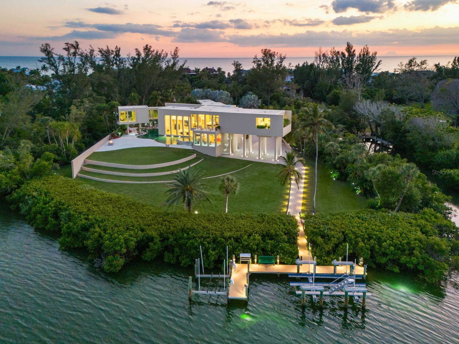 Named the House of Columns by world-renowned, award-winning architect Carl Abbott, this palatial Bayfront estate stands as a singular expression of architectural distinction and craftsmanship. Encompassing close to five acres on the north end of Longboat Key spanning Sarasota Bay, the combined offering of 6610 and 6630 Gulf of Mexico Drive represents one of the most significant residential holdings available in the area, a legacy estate where endless views of sea and sky create an unforgettable backdrop for living. The property unfolds like a private peninsula, offering exceptional width, depth and privacy. On the eastern shoreline, calm bay waters reflect the morning light with open water, protected shoreline and bridgeless access to the Gulf of Mexico. The primary residence is gracefully positioned on the bayfront, designed to capture eastern exposure and long, tranquil water views across Sarasota Bay. Clean architectural lines, soaring interior volumes, and walls of glass create a continuous dialogue between interior and exterior. Ceilings soar up to 21 feet, allowing light to move freely throughout the home while maintaining warmth and livability. The elevator provides access across levels, while Lutron lighting and automated shades on every window and door allow the home to respond intuitively to the changing light of day. The residence has been impeccably maintained by its original owner, reflecting a level of care and stewardship rarely found. Infrastructure has been thoughtfully addressed, including a whole-home generator that ensures continuity and peace of mind. The owner’s garage sits under a cantilever with access to the interior elevator and an additional air-conditioned four-car garage with large workspace offers a total space for 6 cars and exceptional flexibility for collectors, hobbies or future customization. A lagoon-style pool sits within the landscape, offering a resort-like atmosphere while preserving privacy and water views. A private dock with two boat lifts provides immediate access to Sarasota Bay and the Intracoastal Waterway, creating a seamless boating lifestyle that complements the estate’s waterfrontage. The inclusion of 6630 Gulf of Mexico Drive allows owners to construct a guest house or secondary structure, offering flexibility for multigenerational living, guests, or staff accommodations, offering extraordinary future optionality and ensures the next owner retains control over one of Longboat Key’s irreplaceable resources, land. What ultimately distinguishes this offering is its irreplaceability. Estates of this size, with this combination of architectural pedigree, boating infrastructure, development flexibility and maintained condition are no longer being created. Despite its scale and seclusion, you are moments from the refined lifestyle Longboat Key is known for, private clubs, championship golf, fine dining, IMG Academy and the cultural offerings of Anna Maria Island, St. Armands Circle and downtown Sarasota just beyond the bridge. This is not merely a waterfront home, it is a generational legacy, unmatched in design, scale, privacy and location.