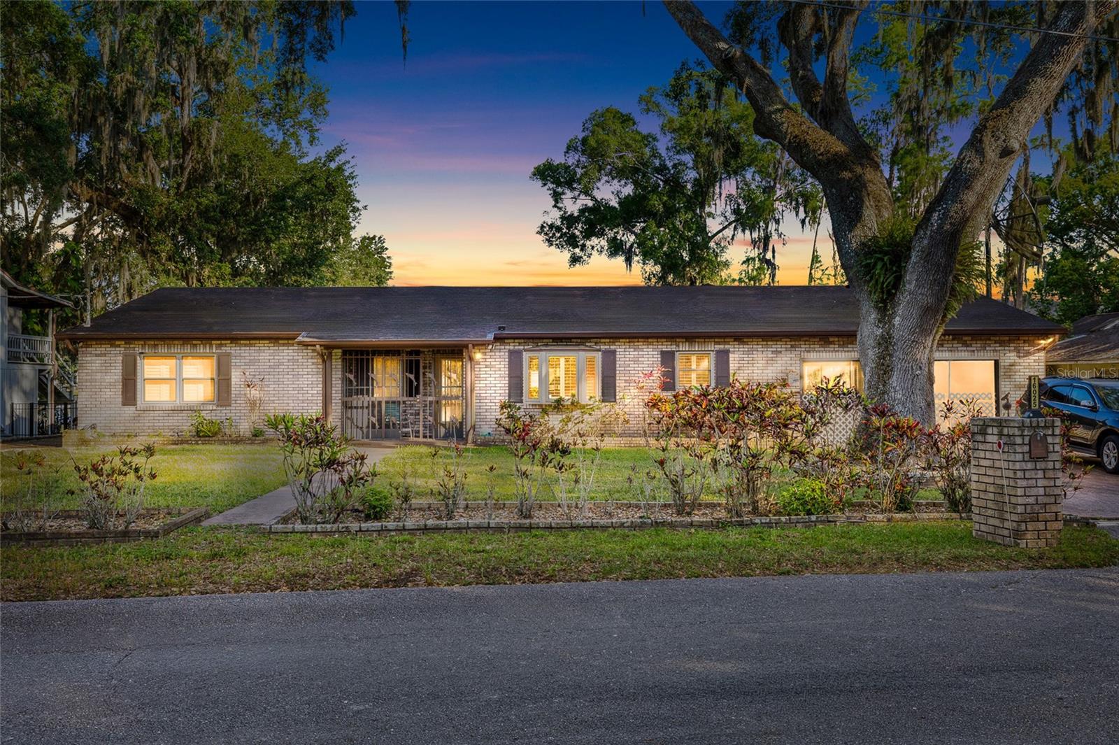 Welcome to a special lakefront retreat where peaceful country living meets everyday convenience. Tucked away on a quiet, tree-lined dead-end drive, this custom Odessa residence offers exceptional privacy and tranquility—yet sits just minutes from the Suncoast Parkway for an easy commute to Tampa and surrounding areas. Set beneath a canopy of majestic oaks, this custom-built brick home exudes warmth, character, and timeless craftsmanship. A charming front porch leads into a lodge-inspired entry leading to the Great Room featuring rich wood walls, a striking stone fireplace, custom built-ins, and generous space for gathering with family and friends. The spacious kitchen offers abundant cabinetry, extensive counter space, a center island, double wall ovens, and an open layout that flows seamlessly into the main living area. Large windows frame beautiful views of the lake, filling the home with natural light. Designed to embrace Florida’s outdoor lifestyle, the expansive screened lanai overlooks the picturesque backyard and sparkling Lake Armistead—perfect for morning coffee, evening sunsets, or year-round entertaining. A private floating dock provides seating area, two roll on lifts for wave runners or small boat or kayaks, and provides easy on and off for boats, paddle boarding, swimming, and some of the best Bass fishing in Hillsborough County.  Moving back inside, an oversized primary suite serves as a peaceful retreat with room for a sitting area. The spacious custom bath featuring dual vanities, a large walk-in shower with glass block accents, a soaking garden tub, and exceptional storage. Cedar-lined walk-in closets add both luxury and practicality. One of the home’s most unique features is the oversized garage, thoughtfully designed with both a traditional front-facing garage door and an additional rear garage door that opens toward the lake. This breezeway-style setup offers unmatched convenience for storing boats, lawn equipment, or creating the ultimate workshop with effortless access to fenced in dog run and the backyard and waterfront. Completing this home are a Generac Whole House Generator, Water Filtration System and Natural Gas Tank. If you’ve been searching for a home that offers privacy, character, generous living spaces, and true waterfront enjoyment—while still being just minutes from shopping, dining, and major highways—this Odessa lakefront property at 16029 Chastain Rd is the opportunity you do not want to miss.