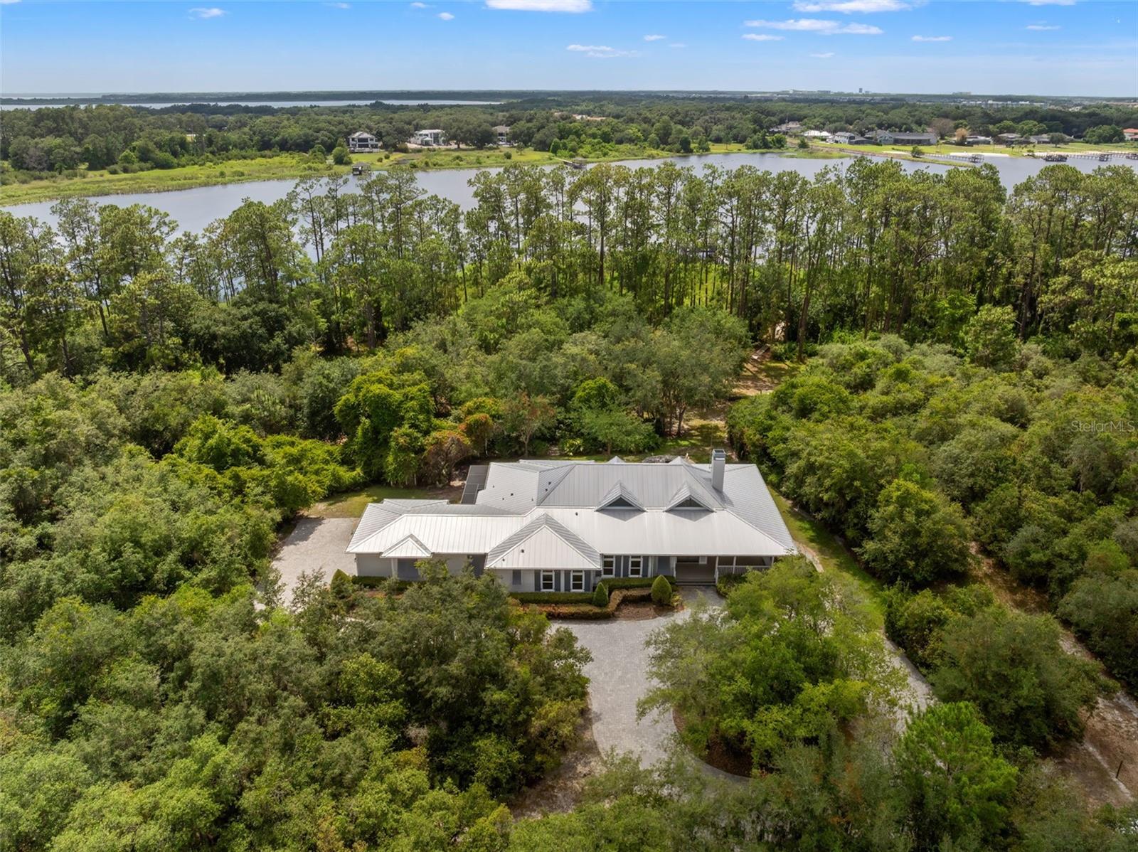 Nestled behind the gates of the exclusive Springhead community of only 5 lots, this exceptional lakefront estate offers the perfect blend of privacy, acreage, and waterfront living. Situated on 3.49 acres along the shores of beautiful Lake Ajay, the property boasts an impressive 247 feet of water frontage and breathtaking views from nearly every angle. Built in 2018, this thoughtfully designed single-story residence features 4 bedrooms, 4 full bathrooms, and 2,974 square feet of heated living space, with a total of 4,698 square feet including expansive covered outdoor living areas and a two-car garage. A welcoming wraparound porch and oversized rear lanai create the perfect setting for enjoying Florida’s outdoor lifestyle year-round. Inside, wood-look tile flooring flows throughout the home, complemented by unique designer light fixtures and a warm gas fireplace that anchors the main living space. The chef-inspired kitchen is both beautiful and functional, featuring two oversized islands, a gas range, abundant cabinetry, and seamless flow into the dining and gathering areas, ideal for entertaining. The spacious primary suite offers a private retreat with serene property views, dual vanities, and a thoughtfully designed ensuite bath. Three additional bedrooms and bathrooms provide comfortable accommodations for family and guests. Outdoor living takes center stage with expansive side and rear porches overlooking the sprawling grounds and lakefront setting. Gather with friends around the outdoor living spaces, or simply enjoy the peace and privacy that come with nearly 3.5 acres of gated waterfront property. Additional highlights include a metal roof, two water heaters, one HVAC system, and a two-car garage. Rarely does a property deliver this combination of acreage, waterfront frontage, modern construction, and gated privacy in such a picturesque setting. Don't miss out on this opportunity!