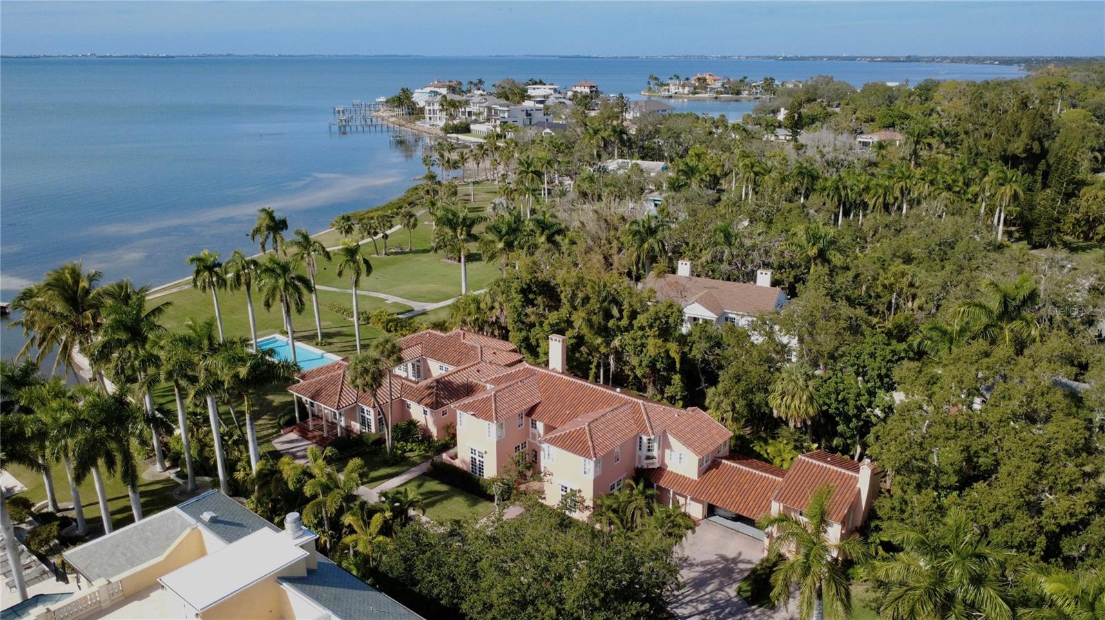 Nestled on 1.1 acres of pristine bayfront along Sarasota Bay, Etowah stands as a timeless icon of Sarasota’s rich architectural heritage, offering sweeping, wide-open bay views to the north and south, from the manicured lawn at the water’s edge all the way to the distant skyline of downtown Sarasota, with glowing sunset views that unfold nightly across the horizon. Originally built in 1925, this distinguished two-story Mediterranean Revival estate spans over 6,500 square feet and commands captivating views across the bay, all while being just 10 minutes from downtown Sarasota. Following an extensive year-long restoration, Etowah has been meticulously renewed from the inside out. Every major system of the home has been comprehensively replaced or upgraded, including all new electrical, plumbing, heating and air-conditioning systems, roofing, insulation, and drywall, ensuring modern performance while preserving historic integrity. A significant west-side addition by renowned local architect Frank Folsom Smith in 1992 introduced a gracious primary suite, a sophisticated bar area, and a grand great room—enhancements that seamlessly complement the home’s historic character. Upon entry, a vaulted ceiling sets a dramatic and welcoming tone, guiding you into the formal living room anchored by the home’s original fireplace. The adjacent dining room, surrounded by windows crafted with original glass sourced from the nearby Ringling era, creates an extraordinary setting for entertaining and comfortably accommodates gatherings of 12 or more. Designed for both elegance and performance, the chef’s kitchen is outfitted with top-of-the-line Thermador appliances, a Sub-Zero refrigerator, and every modern convenience, while the sun-filled eat-in area offers the perfect spot for morning coffee overlooking the grounds. The west wing of the home unfolds around a serene courtyard, with the great room and owner’s suite positioned on either side—creating a seamless indoor-outdoor living experience. The owner’s suite features sweeping bay views, dual walk-in closets, and a spacious spa-like bath. Upstairs, a second primary bedroom offers its own wood-burning fireplace, picturesque bay vistas, and generous closet space. 3 additional bedrooms on this level are well-proportioned and thoughtfully laid out, complemented by a sunken office or den tucked quietly at the end of the hall. The grounds are equally exceptional, highlighted by a heated, resort-style 15’ x 50’ swimming pool—perfect for both relaxation and entertaining. Completing the waterfront setting is a 4’ x 50’ dock, providing direct access to Sarasota Bay for boating, paddleboarding, and waterfront enjoyment. Completing the property is the original detached garage with an adjoining workshop, gardening space, laundry facilities, and private guest quarters—ideal for visitors or staff. A rare offering of architectural significance and modern luxury, Etowah is a one-of-a-kind estate that seamlessly bridges historic Florida elegance with contemporary living, all set against the unparalleled beauty of Sarasota Bay.