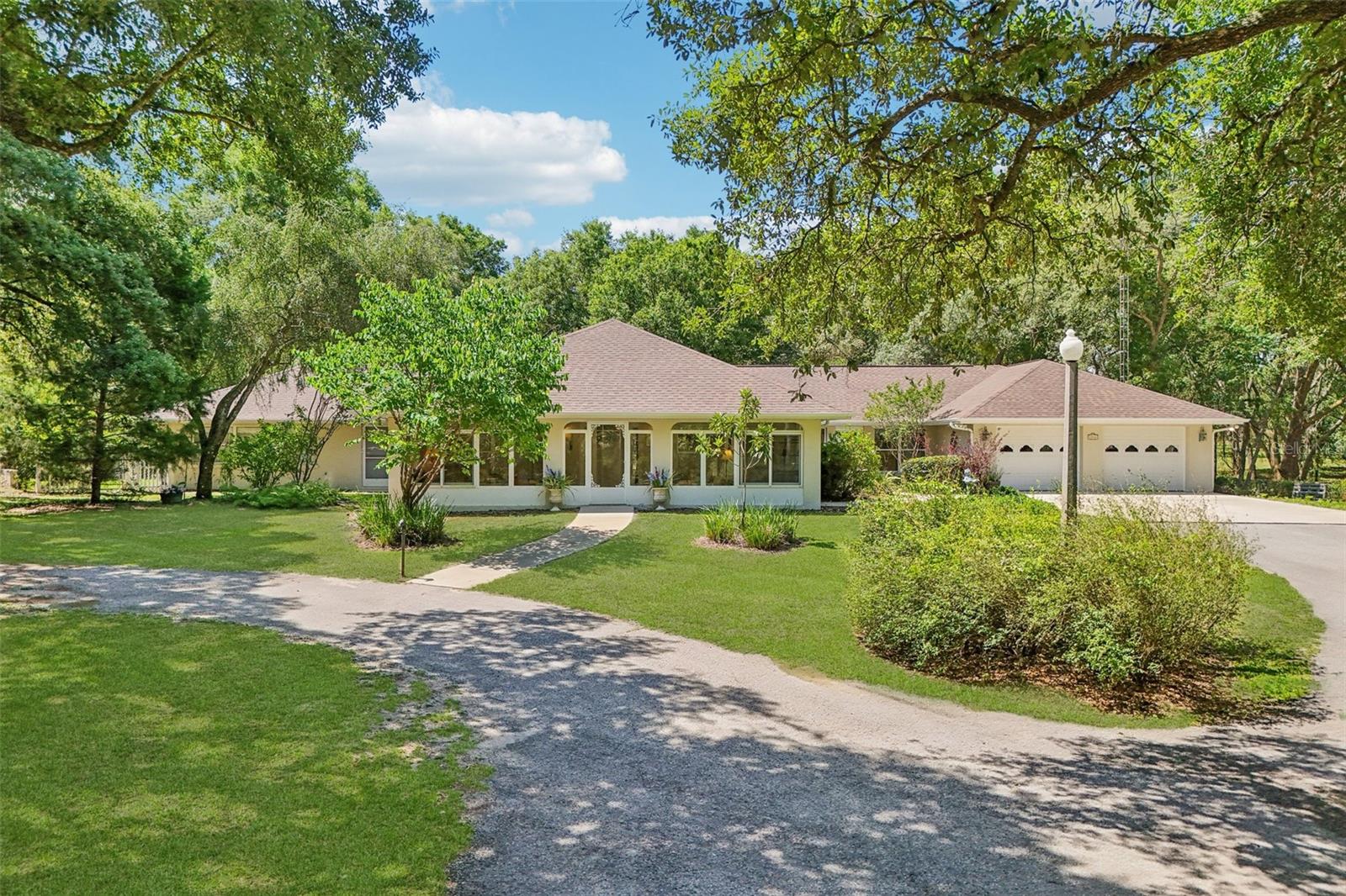 Nestled on approximately 10 partially cleared and fenced acres, this one-of-a-kind country estate offers the perfect blend of privacy, flexibility, and Florida charm. The private drive winding through majestic oaks and lush natural beauty, leads to a quaint retreat welcoming you with a circular drive, a sprawling ranch-style design, and an inviting atmosphere that feels like home from the moment you arrive. Inside, you’ll find expansive living spaces filled with natural light, oversized windows showcasing peaceful views, and ceramic tile flooring throughout the main living areas. The spacious kitchen offers abundant cabinetry, generous counter space, and a sunny breakfast area overlooking the property.  The master suite is breathtaking, with it's large sitting room, ensuite bath, and private lanai. The versatile game room presents exciting possibilities for multigenerational living or guest accommodations. With its own private entrance off the breezeway, direct access to the rear patio, and a nearby full bath with shower access independent from the main house, the space could easily be transformed into a private in-law suite, guest retreat, or home office. The breezeway itself offers additional potential as a cozy sitting area or relaxing nook. The oversized back patio is a true highlight—vast and versatile, it’s ideal for outdoor gatherings, dining al fresco, or simply soaking in the serene views. Imagine the possibilities—with its expansive footprint, there’s plenty of room to add a pool with a screened birdcage, creating your own private oasis. Nestled in a lovely flower garden, a screened retreat featuring metal roof, lights, and a ceiling fan provides the perfect hideaway for relaxing with your favorite book, or for an intimate dinner for two. Recent updates ensure peace of mind, including a new roof installed in December 2024, new ductwork and an ultraviolet filtration HVAC system installed in October 2025, and energy-efficient double-pane aluminum windows. Two concrete block outbuildings currently serve as storage sheds but present endless potential for a workshop, extra storage or even a guest cottage. Whether you dream of multigenerational living, a private homestead, or simply room to grow, this exceptional property is a rare find. Select furnishings and antiques may be available under separate negotiation. Call listing agent for a private tour. Video tours available for Out-of-town buyers.