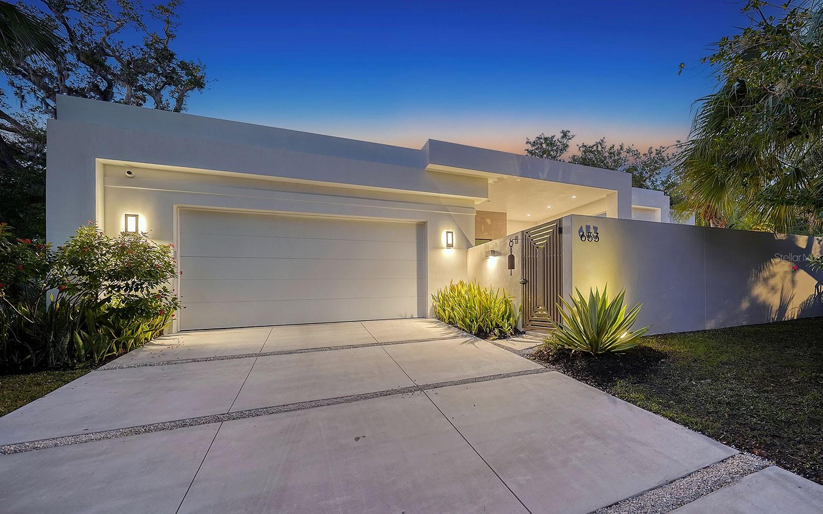 Exquisite Sarasota Modern nearly-new luxury home, mindfully constructed in 2021 incorporating the latest in design and technology features. A commitment to quality craftsmanship is evident throughout with an emphasis on creating spaces that promote relaxation and well-being. Every detail embodies a unified approach to perception, ease and affinity with the natural surrounds. Best-in-class construction and design features include concrete block construction, oversize impact glass throughout, high ceilings, smart home integration, generator, in-cabinet electrical outlets, true north art studio and climate-controlled storage room. At the heart of the 3,200-square-foot home is an expansive social space that incorporates kitchen, dining and living areas with wall-to-wall sliding glass doors to the covered lanai and outdoor kitchen. Designed by a former cook, the kitchen is a culinary delight. Clad in a calming mix of muted colors, it features Italian two-toned cabinetry, quartz countertops, stainless steel kickplates, high-end appliances, generous storage, a massive eat-in island and walk-in pantry. Private retreats include two-bedroom suites plus two additional bedrooms being used as a home office and art studio. A standout feature of the property is the primary suite, which opens to the outdoor serenity patio. It includes dual walk-in closets, and a luxurious en-suite bath with dual vanities, dressing mirrors, a curb-less walk-in shower and full-light door to an outdoor shower. Beautifully finished living spaces extend beyond the exterior walls to outdoor spaces that surround the residence. A courtyard entry with water chain and water fountain creates a stunning entry as well as an inspiring extension of the home office. The primary suite opens to a serene patio with a Bullfrog jetted spa and outdoor shower ensconced by a natural wall of Mast trees. The great room opens to a substantial 680-square-foot covered lanai with automated screens and a natural-flame fire table. Set on a .41-acre lot, the property boasts ample outdoor space for enjoying the outdoors. The fully fenced and gated backyard features a heated saltwater swimming pool, and tropical privacy landscape with filtered sunlight from several mature oak trees. Indian Beach offers an idyllic setting that’s merely seven minutes north of downtown Sarasota’s urban hub. This singular property offers a peaceful retreat with spacious sheltered spaces that let you find joy in everyday living.