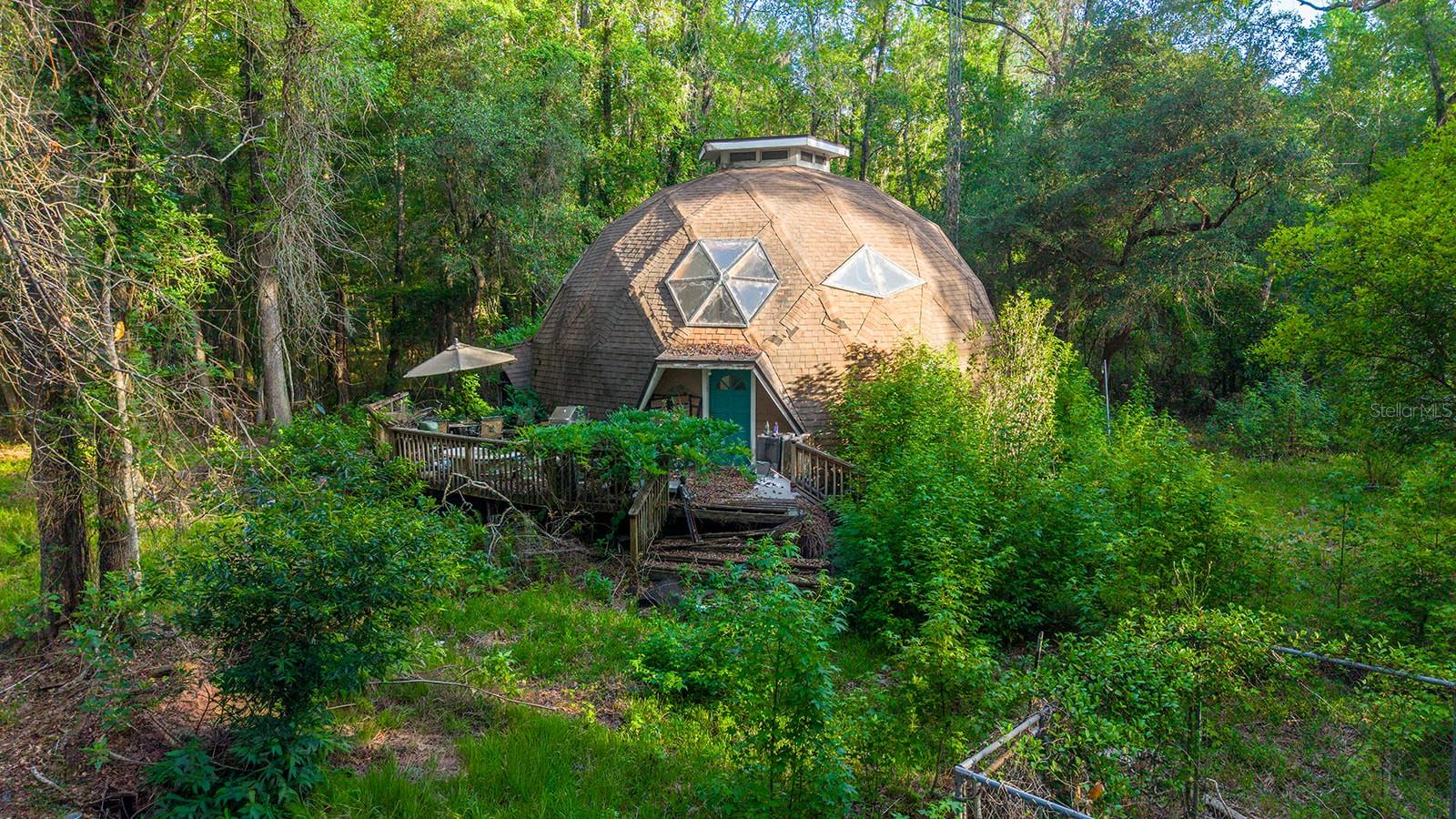 Investment opportunity! Tucked away on 12 beautifully wooded acres is this one-of-a-kind Geodesic Dome Home. Highly energy efficient, and notoriously weather resistant, this is the perfect 'Florida home.' This property is a rare opportunity for those seeking a secluded retreat, homestead, investment property, or a creative renovation project. Though currently dry, this property features a small babbling creek that cuts through the property, and several mature citrus bearing trees. Sale includes 3 parcels total, which may qualify for impact fee waivers if developed. Just 20 minutes from Gainesville, you'll enjoy country living without sacrificing convenience. Home will need a full renovation, all personal property on site is included. A fully-running, registered, & converted 'Skoolie' bus is negotiable as well.