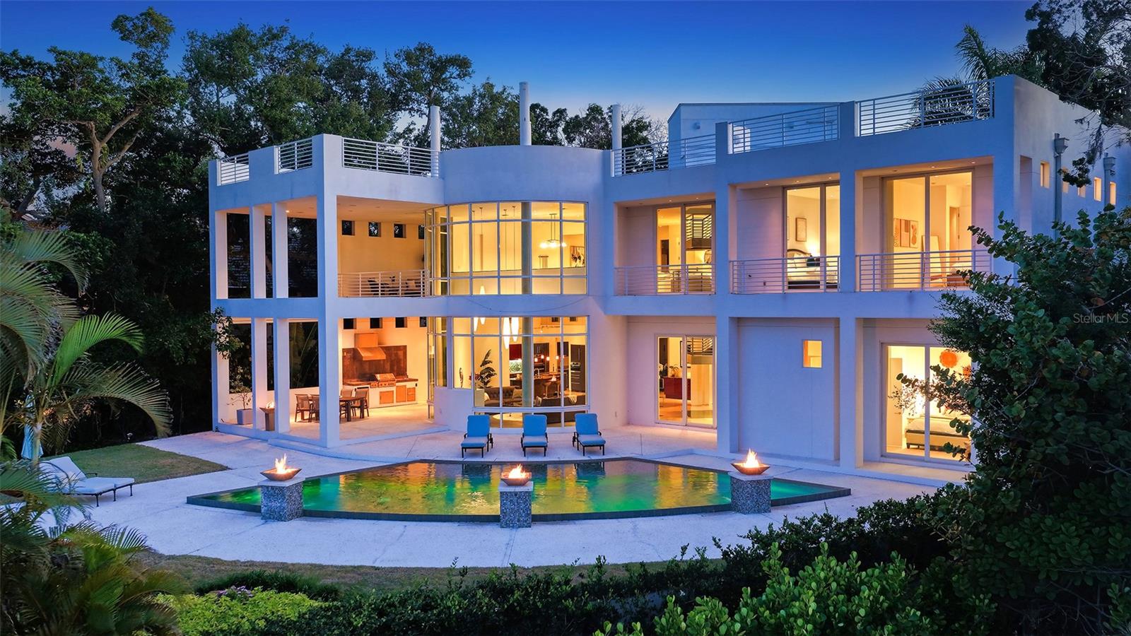 One or more photo(s) has been virtually staged. Celebrated as one of SRQ Magazine’s “Home of the Year” in 2008 and born from the visionary imagination of acclaimed architect Mark Sultana and built by Voigt Construction, this extraordinary waterfront estate is not simply a home — it is a lifestyle. One of Siesta Key’s most iconic private residences, it stands as a living testament to the art of inspired modern design and the art of living beautifully.

Deeply set on nearly one private acre along the tranquil Coconut Bayou, this gated 4-bedroom architectural masterpiece unfolds across multiple stories with absolute privacy, lush tropical splendor, and grounds generous enough for a pickleball court — all anchored by a fully separate guest house for family and friends who will never want to leave.

From the moment the gates open, life here feels different. A breathtaking composition of glass, steel, and sculptural lines soars beneath dramatic ceilings, with natural light pouring through at every angle — whether that’s a lazy Sunday morning or a dinner party in full swing. Rise by private elevator or ascend the sweeping steel-and-glass staircase to the crown jewel of this residence: a 2,500 sq. ft. rooftop terrace, where the Siesta Key lifestyle reaches its absolute peak. Panoramic views sweep across Siesta Key, the downtown Sarasota skyline, and the shimmering waterways below — this is where memories are made.

At the water’s edge, a brand-new dock on order, a double jet ski lift, and a dedicated kayak and paddleboard launch await — with direct, bridge-free access to the Intracoastal and the open Gulf beyond. This is the rare address that refuses to make you choose: the serenity of bayfront living, the thrill of open-water boating, and the privilege of private deeded beach access to the shores of Siesta Key — all from a single extraordinary estate.

Designed with both beauty and resilience in mind, the residence sits impressively high and dry above the Bayou. Even through recent storms, the property remained untouched by flooding — including the pool area — offering a rare sense of peace of mind along Sarasota’s waterfront.

The primary suite is a private world of its own — featuring a dedicated office/loft or exercise room, two custom walk-in closets, and a private balcony suspended above the Bayou. At the center of it all, an indulgent Champagne Jacuzzi infinity bathtub transforms every evening into a spa retreat. Downstairs, entertaining flows as naturally as conversation — from a dedicated movie theater room to tiered outdoor patios crowned by a spectacular summer kitchen, an open saltwater pool, and glowing fire bowl accents that keep the night alive.

In the kitchen, Italian custom cabinetry, top-tier appliances, a service pantry, and a private wine cellar come together in a space as pleasurable to cook in as it is to gather around. Garage parking for five vehicles and separate guest quarters complete an offering with virtually nothing left to wish for.

Minutes from The Out-of-Door Academy, Siesta Key Village, and Siesta Beach — this is not just an address. It is a life you’ll never want to leave.