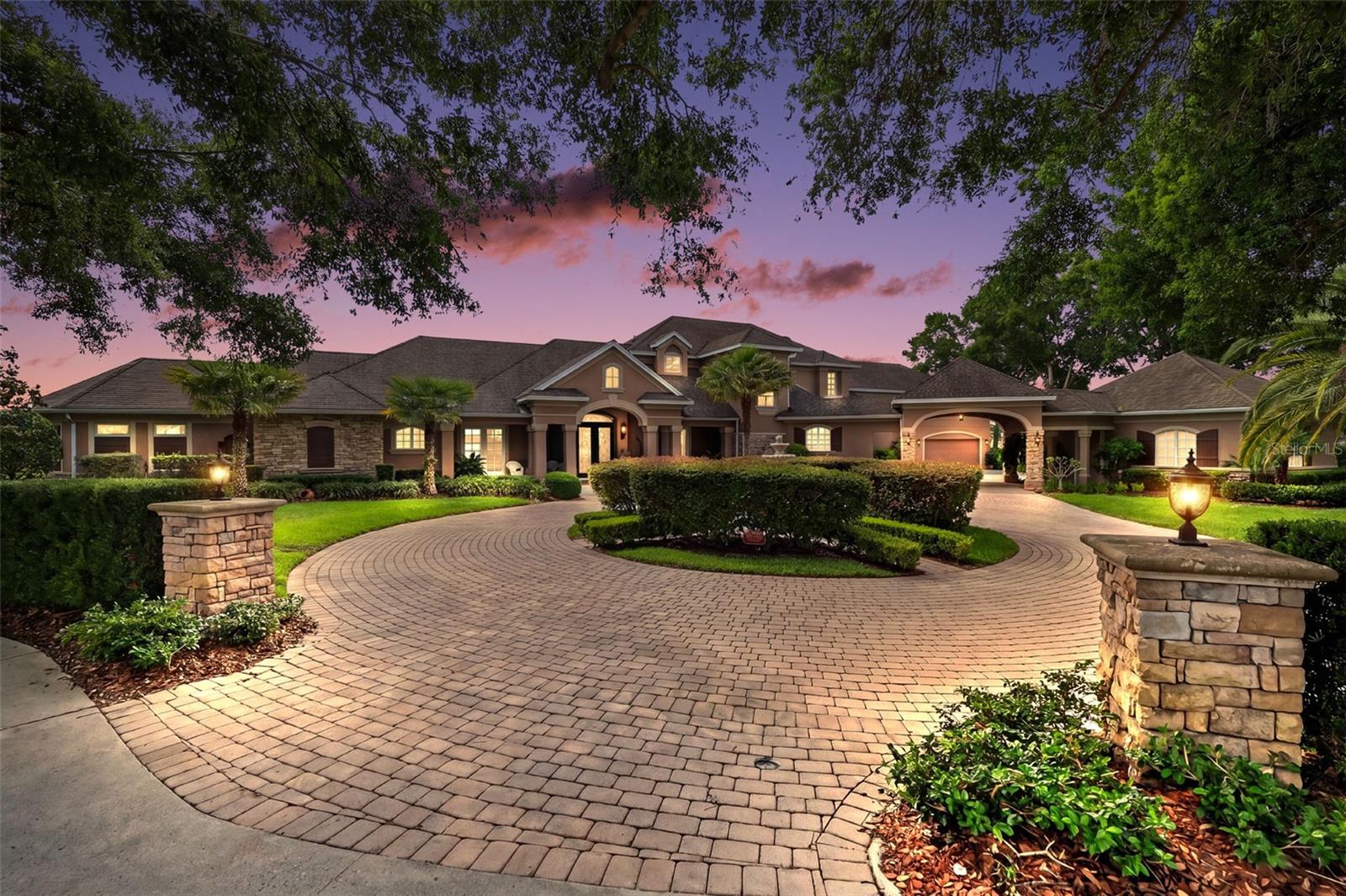 Located in the exclusive gated community of Loch Leven in Mount Dora, this extraordinary custom lakefront estate offers luxury living with breathtaking panoramic views of spring-fed Lake Loch Leven. Situated on 4.55 acres with approximately 200 feet of waterfront frontage, this impressive residence features over 5,600 square feet of thoughtfully designed living space with 5 bedrooms, 4.5 bathrooms, multiple flex spaces, and resort-style outdoor amenities.
From the moment you arrive, the circular paver driveway, porte cochere, stone accents and 2-two car garages create a grand first impression. Elegant leaded glass front doors welcome you into a stunning interior showcasing soaring ceilings, travertine and oak flooring, archways, crown molding, and expansive lake views throughout. The inviting family room features a gas fireplace, dramatic coffered wood ceilings, and spectacular lake views, creating a warm yet elegant gathering space. The spacious chef’s kitchen appointed with granite countertops, stainless steel appliances, gas cooktop, breakfast bar, solid wood cabinetry, and an open layout ideal for entertaining. Multiple living, dining spaces and wet bar flow seamlessly to the outdoor living areas, where an edge-less heated pool & spa, screened lanai, outdoor kitchenette and oversized boat dock with boat slip create the ultimate waterfront retreat.
The thoughtfully designed main floor includes a half bathroom, laundry room, private den/office/library, guest bedroom, full bathroom and office space with direct pool and lanai access, perfectly situated for in-law or guest quarters. The spacious primary suite offers a bonus sitting room, French doors leading to the pool and lanai, walk-in closet, and luxurious ensuite bathroom complete with dual vanities, water closet, walk-in shower, and whirlpool tub.
Upstairs offers 3 additional bedrooms, 2 full bathrooms, storage room and a private movie theater with balcony seating, projector, dumb waiter, ice maker and bar refrigerator. 
Other features include 4 HVAC systems, 2 hot water heaters, new roof 2014, boathouse roof 2020, Simply safe security system, EV charger, Safe room, and abundant storage throughout. The 2-two car garages, covered area, and extended parking offers plenty of room for your toys, family and guests.  Enjoy boating, skiing, and sunset views from your backyard while also taking advantage of Loch Leven’s community amenities including gated entry, tennis courts, playground, and private boat launch. Conveniently located just minutes from historic downtown Mount Dora’s restaurants, shops, and festivals, this exceptional property offers the perfect blend of elegance, privacy, and Florida lakefront living. Some furnishings are negotiable.
