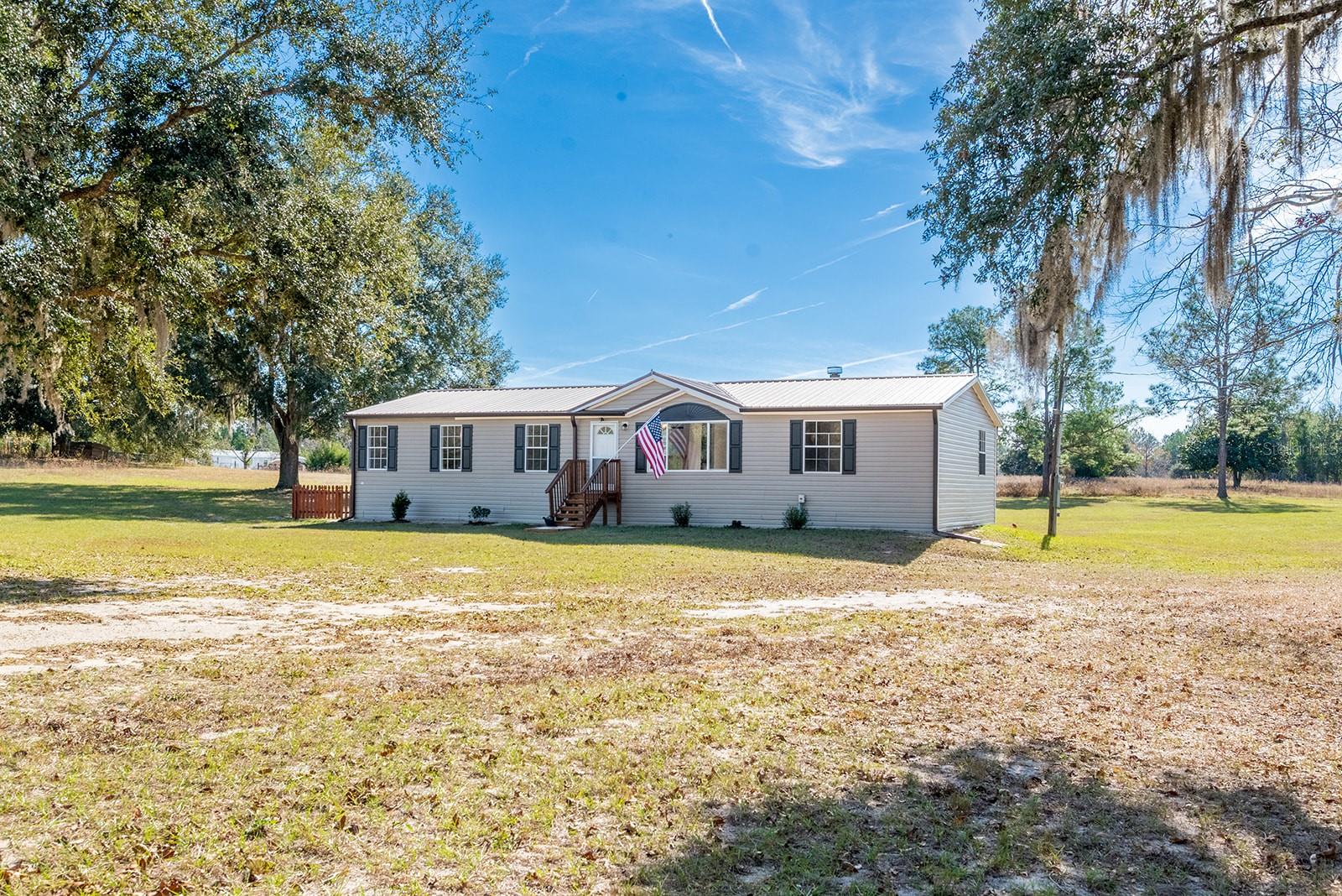 Welcome to this well-maintained 3-bedroom home with an additional office/flex space, perfectly situated on 5 peaceful acres in Trenton, FL. Step inside to find a warm and inviting living area centered around a cozy wood-burning fireplace, creating the perfect gathering spot for family and friends. The interior layout offers a comfortable flow with spacious bedrooms, a versatile flex room ideal for a home office or hobby space, and well-kept finishes throughout. The property is fully fenced and thoughtfully set up for a rural lifestyle. Outside, you’ll find a small chicken coop and a 10x30 pig pen, making it ideal for small livestock or hobby farming. Recent improvements include a new well pump and chlorinator system, as well as an AC replacement in 2021, giving future owners added peace of mind. Just steps away is Christmas Lake, a serene community lake that residents have access to—perfect for quiet mornings, peaceful walks, or simply enjoying the natural beauty of the area. With its blend of comfort, space, updates, and true country living—while still being close to the conveniences of Trenton—this property offers an ideal place to call home.