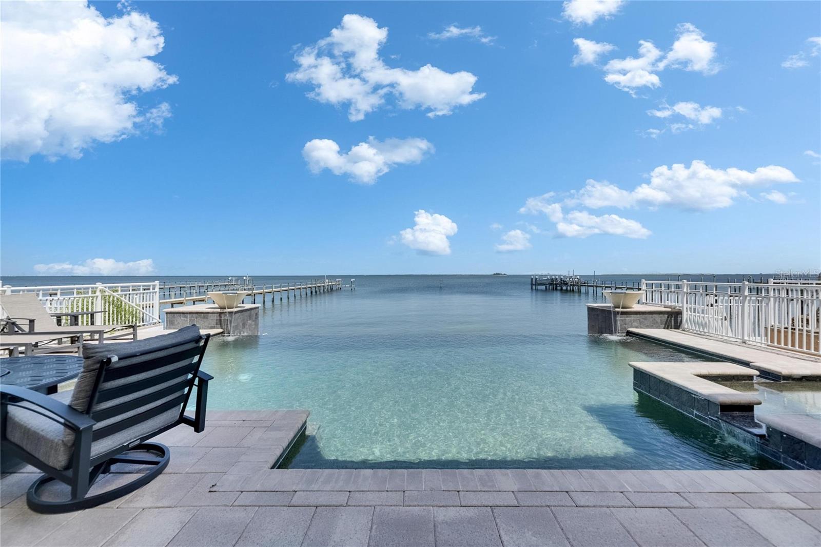 Experience luxury coastal living in this breathtaking Spanish Mediterranean home, perfectly positioned in an exclusive gated community to capture UNOBSTRUCTED PANORAMIC VIEWS of Tampa Bay, St. Petersburg and the Skyway Bridge. As you step through the newly installed custom front door, you're immediately drawn to the show-stopping heated infinity-edge pool and spa that visually blend into the sparkling waters beyond.  From nearly every room, enjoy mesmerizing, wide open waters views. A daily reminder of the beauty and serenity this home offers.  Whether you are lounging by the pool, dining al fresco outside the covered outdoor living area, or relaxing on one of the many private balconies, you'll have a front-row seat to the SPECTACULAR SUNSETS that paint the sky in brilliant shades of orange, pink, and gold.  The OUTDOOR KITCHEN completes the perfect setting for unforgettable evenings spent with family and friends. Inside, the elegance continues with a formal dining room and a designer kitchen featuring QUARTZITE COUNTERTOPS, custom backsplash, solid wood cabinets,  butler's pantry, and premium THERMADOR AND SUB-ZERO appliances, including a professional gas range. Wine connoisseurs with certainly enjoy the wine cellar off the kitchen. The main floor also includes a spacious bedroom with full ensuite bath--ideal as a second primary suite--along with a half bath for guests, and a separate private office making working from home a breeze.  The owner's retreat is a true sanctuary with tray ceilings, custom closets, sliders that lead out to a large covered private balcony, and jaw-dropping views.  The luxurious ensuite bath features dual vanities, a soaking jetted tub, and a walk-in shower.  Three additional bedrooms-each with access to private balconies-giving plenty of space for family or guest, with a full laundry room conveniently located on the same level.  Built with durable and energy-efficient ICF (Insulated Concrete Form) construction, the home has been thoughtfully upgraded with new impact-resistant windows (May 2025), two new A/C units, an on-demand tankless water heater, and a new front door (May 2025). This propoerty qualifies as a SHORT-TERM RENTAL, making it as versatile as it is stunning.  Whether you're searching for your forever home or a high-performing investment, this one-of-a-kind waterfront oasis delivers on every level. Easy commute to downtown Tampa (22 miles) and Tampa International Airport (27 miles)
