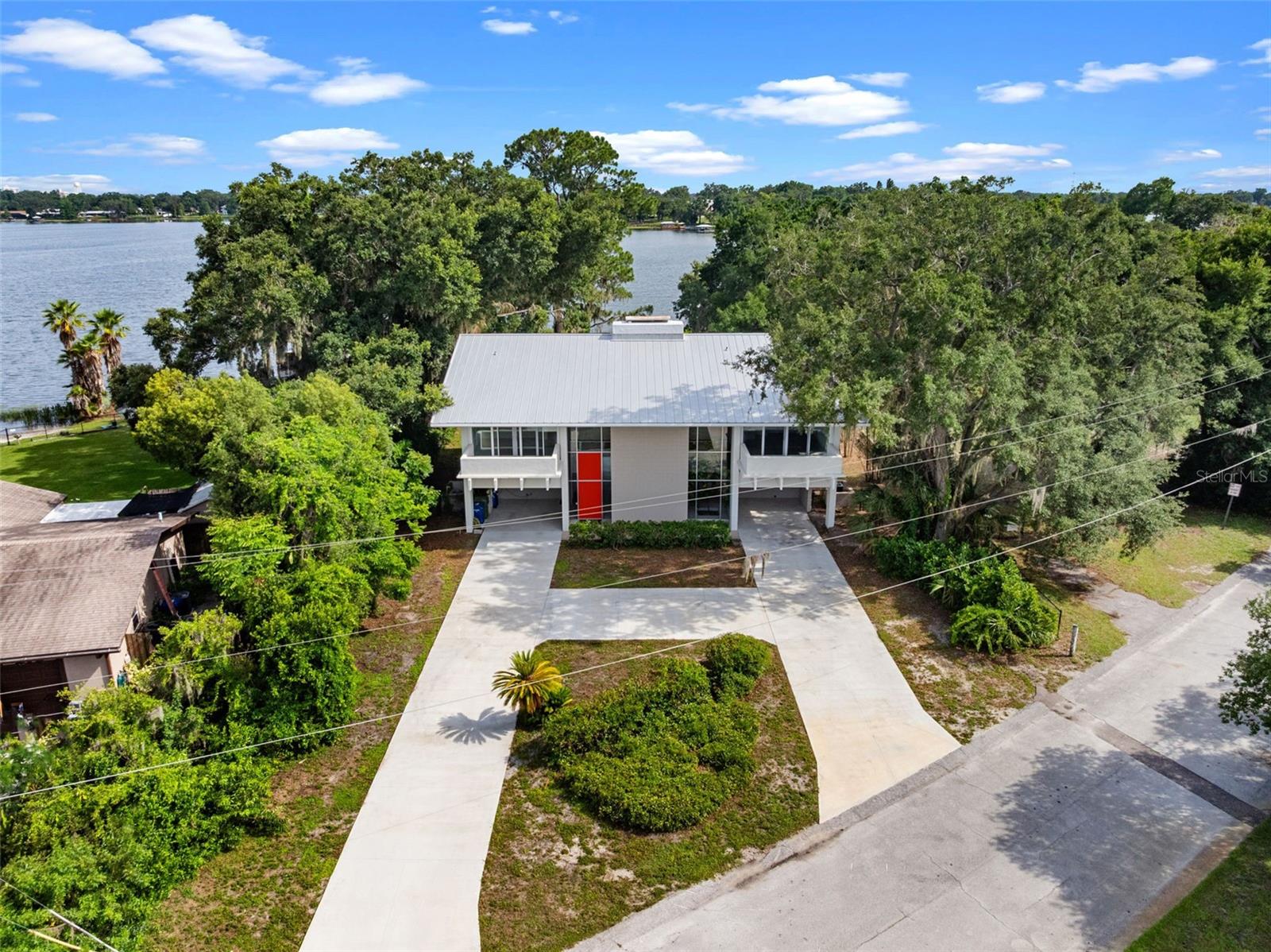 Lakefront living on the Winter Haven Chain of Lakes takes on a completely different feel at The Guest House, a rare Mid-Century Modern residence designed and built by internationally recognized architect Gene Leedy. Quietly tucked away at the end of a cul-de-sac on the crystal-clear waters of Lake Mirror, the setting feels surprisingly hidden despite being just minutes from shopping, dining, and
convenient access to Lakeland, the Polk Parkway, and Interstate 4 for an easy commute between Tampa and Orlando. Originally commissioned for Thelma Guest, "The Guest House" is a striking example of Leedy’s signature architectural style, blending precast concrete construction, dramatic cantilevered forms, walls of glass windows and doors, deep overhangs, and natural light in a way that still feels timeless today. From the street, the design sits perfectly among mature trees and lush landscaping, setting the stage for what awaits inside. The layout was thoughtfully designed around openness, symmetry, and connection to the outdoors. A towering two-story glass entry and interior atrium create an immediate architectural focal point, while the open staircase and original vintage elevator add both character and functionality between levels. The main living spaces are positioned upstairs to maximize natural light and elevated lake views, with expansive glass overlooking the pool, shoreline, and towering oaks draped in Spanish moss. Nearly every upstairs bedroom and living area opens onto long covered balconies, creating seamless indoor and outdoor living. Downstairs offers an entirely different experience with additional flexible living areas surrounding the central atrium and opening directly to the lakefront grounds and pool area . The heated salt-filtered pool feels perfectly integrated into the original architecture, framed by Leedy’s iconic double “T” beam design and expansive covered patios that naturally extend the living space outdoors. The clean geometry, broad overhangs, and shaded entertaining areas create a resort-like atmosphere that feels both private and connected to the lakefront setting.
The property itself offers direct frontage on beautiful Lake Mirror , known for its clear water, scenic shoreline, and access to the larger Winter Haven Chain of Lakes — a connected system of more than 20 lakes popular for boating, skiing, fishing, waterfront dining, and exploring by water. A lightly used public boat ramp located immediately next door makes launching effortless without sacrificing usable
shoreline space on the property itself. Additional highlights include solar panels, tasteful modern updates, integrated storage and closet systems true to the Mid-Century aesthetic, two covered carports, circular drive, low-maintenance landscaping, and no HOA restrictions. Rarely does a home combine architectural significance, true Chain of Lakes waterfront living, privacy, and Central Florida convenience in such a compelling way. The Guest House is more than a lakefront residence — it is a piece of Winter Haven architectural history.