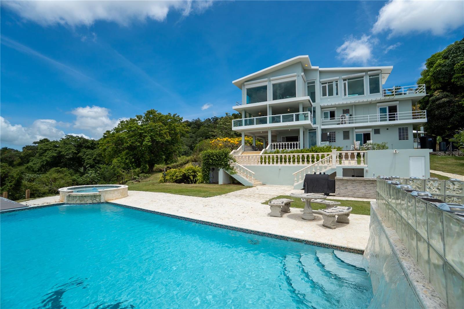 Private Estate Residence in Canóvanas 

Discover a truly unique three-level estate residence located in the Palma Sola area of Canóvanas, designed for those seeking privacy, spacious living, and a resort-style lifestyle without leaving home. This exceptional property combines generous interior spaces, multiple entertainment areas, and amenities rarely found in a single residence.

Featuring approximately 5,210 square feet of living space, 5 bedrooms, 5 bathrooms, and a 7,860.79-square-meter lot, this property offers an impressive presence and an ideal layout for large families, executives, or buyers seeking a multigenerational living arrangement.

The residence includes covered and open terraces, expansive balconies, a heated swimming pool, pool bathroom, BBQ area, gazebo, bar area, game room, private theater, elevator, backup generator, water cistern, photovoltaic solar system, and ample storage areas. In addition, it features a separate apartment with its own private entrance, perfect for guests, extended family, a private office, or other flexible uses.

Its reinforced concrete and concrete block construction provides durability and long-term value, while the outdoor spaces invite you to enjoy the views, entertain guests, and relax in complete privacy.

Located in a peaceful rural-residential setting with convenient access to schools, hospitals, shopping centers, and recreational facilities, this property offers the perfect balance of tranquility, accessibility, and exclusivity.

This estate-style residence is ideal for buyers seeking more than just a home—they are seeking space, privacy, entertainment, and an elevated lifestyle.