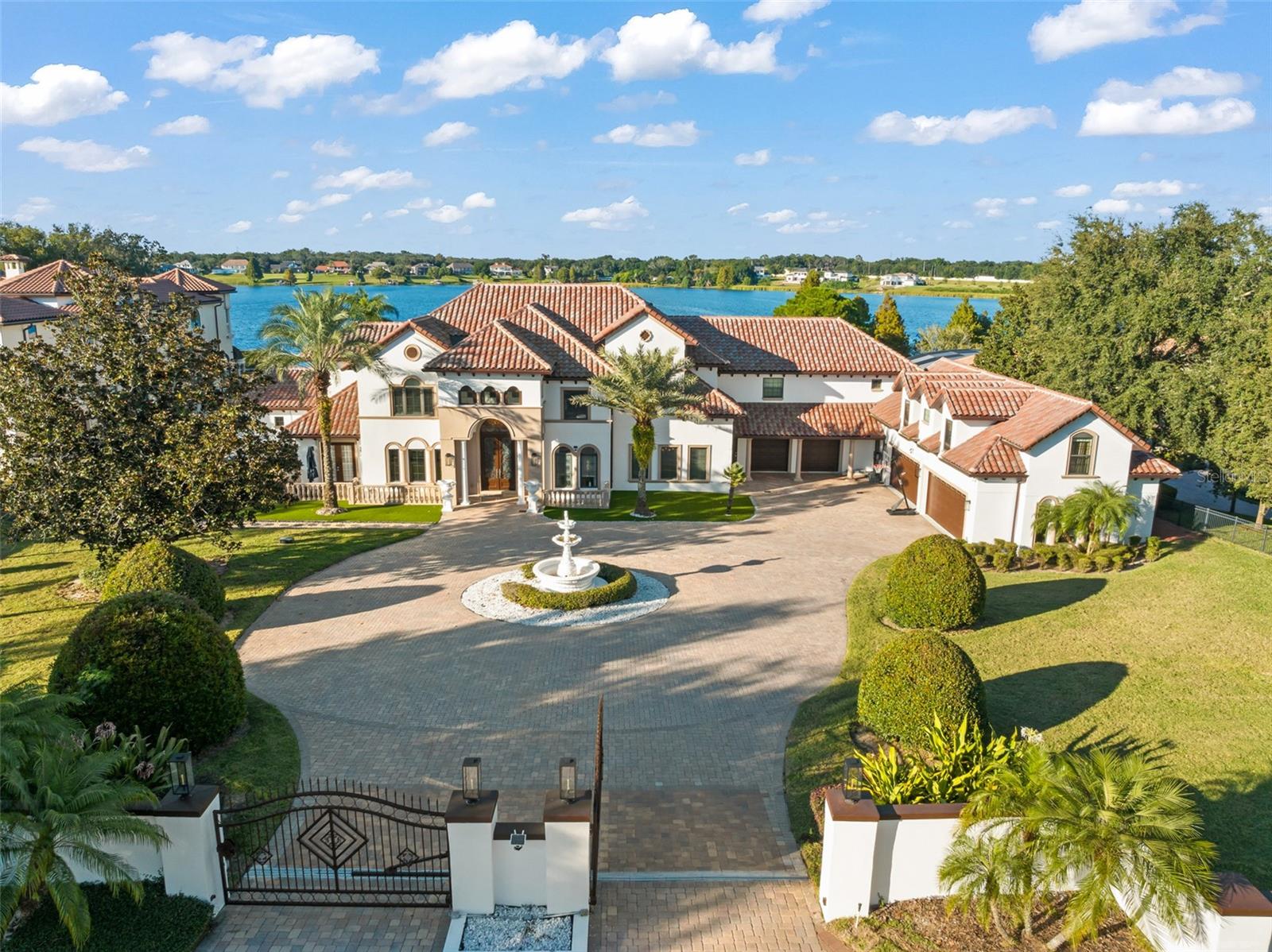 Discover “Bella Olivia”: a grand mediterranean estate perched high above Lake Olivia showcasing sweeping lake views, private gates, and an expansive luxury residence spanning over 8,900 square feet of living space across 7 bedrooms, including two primary suites, two guest apartments, garage space for 6 cars, an enormous screened enclosure with resort-style pool and spa, over 5.4 acres and no HOA.  This private palace with brand new roof impresses with large circular paver drive, 3-tiered fountain, 10-foot iron front doors, 35-foot high ceilings, custom iron railings, and marble and travertine flooring – plus, coffered ceilings and elegant details throughout.  Home has been extensively updated and lovingly cared for to highlight classic style and luxury to compliment today’s sophisticated lifestyle. The main kitchen features beautiful marble counters, three islands, two preparation sinks, custom cabinetry, and stainless appliances including two dishwashers, two microwaves, double ovens, and a Viking gas stove. The first-floor primary retreat is dressed with hardwood flooring, tray ceiling, and triple crown molding, and an exceptional bathroom with tiled shower, jetted tub, dual vanities, and expansive double closets. The main living spaces are abundant and stately with two first-floor family rooms, billiards room, living room, dining room, theater, and guest suite – upstairs is a third family room, secondary master suite, and three additional guest suites, plus a large balcony with screens.  A separate entrance off the kitchen provides access to a private guest apartment with a kitchenette, family room, and bedroom.  Plus, a second private apartment (978 sq feet, not included in the listed 8,931 sq feet) is accessible from the outside and is located over the 4-car garage and features family room, sink, and bedroom.  Functional outdoor living space is extended to the mammoth screened enclosure to encompass a sitting area off the master and an additional family room with fireplace, tv, and full summer kitchen across the pool deck that can be separated by an electric additional privacy screen. The showstopping infinity edge pool is colossal in size and includes a sun shelf for shallow water relaxing and an infinity hot tub.  Both sides of the house have all been paved with a new drainage system and ramps for easy access for boats and watercraft to Lake Olivia. The 150 ft refreshed covered dock has two cradles: currently set for a boat and two jet skis.  There’s also a sitting area for lounging lakeside. Experience the best of Windermere with this lakefront retreat built for privacy, luxury, and lifestyle.