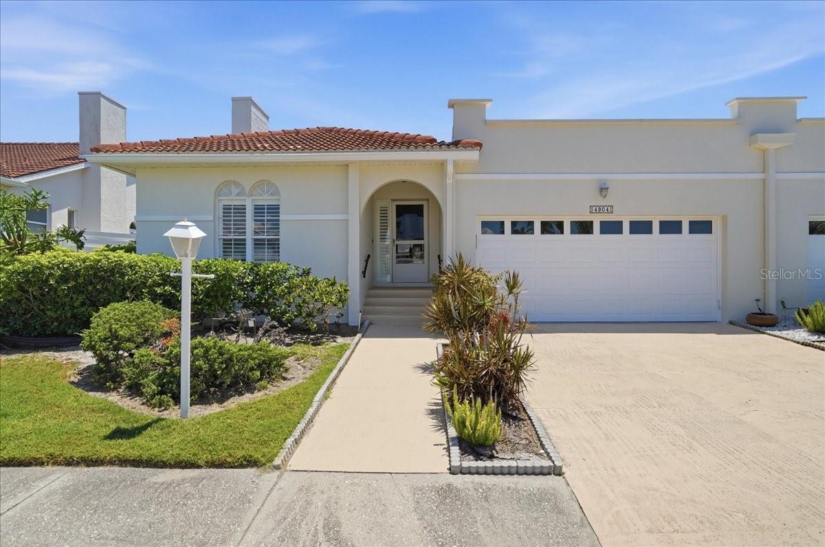 Meticulously maintained villa tucked at the end of a private cul-de-sac in the highly desirable Palm Court community. This home welcomes you with an expansive, light-filled open floor plan and tasteful finishes throughout — tile floors for easy maintenance, soaring vaulted ceilings that amplify the sense of space, and plantation shutters that add a refined, coastal-Florida touch to every room. Enter into a flexible living layout designed for comfortable daily living and effortless entertaining. To the left, a versatile den provides a private retreat or home office and is appointed with a convenient wet bar and a closet that can be easily converted to a third bedroom if desired, offering adaptability to suit your lifestyle. The generous guest bedroom benefits from ample natural light and a bright, airy ambiance. At the heart of the home is an oversized living room that seamlessly connects to an enclosed under-air lanai — an ideal spot for morning coffee, relaxing with a book, or hosting guests in comfort year-round. The kitchen is thoughtfully laid out for both everyday meals and gourmet pursuits, featuring countertop seating for casual dining and a gas range that will delight any avid chef. Sliding glass doors off the kitchen open to a covered patio where you can unwind and enjoy views of your private, fenced backyard — perfect for pets, gardening, or al fresco entertaining. The primary suite is a peaceful sanctuary flooded with natural light and direct access via sliders to the Florida room, expanding your indoor/outdoor living options. It also offers a roomy walk-in closet and an ensuite bathroom with an oversized shower, designed for relaxation and convenience. Throughout the home, vaulted ceilings enhance the airy, open feel and contribute to the inviting flow of the floor plan. Beyond the property, Palm Court is a quiet, well-kept community renowned for its tranquil streets and neighborly atmosphere. This location places you moments from IMG Academy golf facilities, a short drive to the world-class beaches of Anna Maria Island, and close to a rich selection of restaurants, shops, and local amenities. Whether you’re seeking a full-time residence, or a seasonal retreat this villa offers an exceptional combination of style, comfort, and Florida lifestyle living.