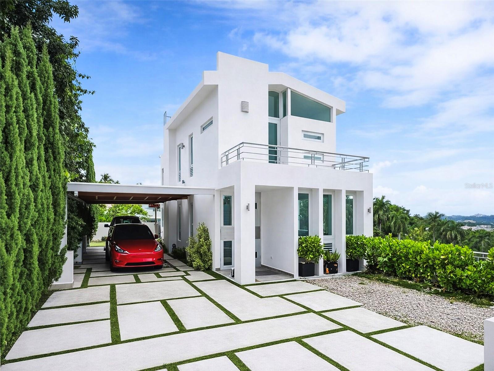 One or more photo(s) has been virtually staged. An Iconic Contemporary Residence with Lush Green & Ocean Views | La Floresta, Bayamón

Gracefully elevated above the landscape of La Floresta, Bayamón, this contemporary residence, stands as a refined architectural statement designed to engage its natural surroundings. Developed across four distinct levels, the home captures expansive green vistas with distant ocean views, offering an exceptional sense of privacy, serenity, and architectural sophistication.

Every line, volume, and transition has been thoughtfully conceived to frame light, air, and landscape, allowing the environment to become an integral part of the living experience.

Property Specifications:
Gross Living Area: 3,976 sq ft;
Total Construction Area: 5,877 sq ft;
Lot Size: 1,053 sqm;
Bedrooms: 4;
Bathrooms: 5 (full);
Levels: 4 (prepared with elevator space);
Year Built: 2016.

Architecture & Interior Design:
The interior reveals a timeless minimalist aesthetic, defined by generous proportions, clean lines, and seamless spatial flow:
A sleek contemporary main kitchen, featuring custom cabinetry, quartz surfaces, stainless-steel appliances, and large windows that frame verdant views while flooding the space with natural light;
Open-concept living, dining, and family areas, enhanced by large-format tile flooring that adds continuity and understated elegance;
Independent laundry room;
A flexible auxiliary space ideal for a wine cellar, private office, or executive study;
Each level unfolds as a carefully orchestrated sequence of spaces, balancing openness and intimacy with architectural precision.

Private Suites:
The Primary Suite, conceived as a private sanctuary, features:
A spa-inspired en-suite bathroom;
Walk-in closet;
Direct access to a private balcony and terrace;
Sweeping green and ocean-horizon views, creating a tranquil retreat.

A Junior Suite, offering:
En-suite bathroom;
Private terrace immersed in the surrounding landscape.

Additional bedrooms are spacious, light-filled, and well-ventilated, each enjoying views toward the lush natural setting and with it's own balcony.

Bathrooms throughout the residence reflect a refined, contemporary design with walk-in showers, modern fixtures, and carefully selected finishes.

Entertainment Level
The lower level has been masterfully designed as a self-contained entertainment and social retreat, perfect for hosting in absolute privacy:
Lounge-style living area,
Secondary kitchen,
Dining area and media space,
Full bathroom,
Direct access to outdoor terraces,
This level allows for effortless entertaining without disrupting the home’s private living quarters.

Outdoor Living & Amenities:
Swimming pool with swim jets, ideal for stationary lap swimming and relaxation, set against a lush green backdrop.
Two expansive terraces with pergola, outdoor lounge and dining areas.
Modern balconies, offering panoramic views of the surrounding greenery and ocean.
Thoughtfully integrated landscaping and exterior walkways that complement the architecture with understated elegance.

The Experience:
More than a residence, this property is a curated architectural experience— with contemporary design, spatial sophistication, and a privileged natural setting converge to deliver an exclusive, serene, and elevated lifestyle.

An exceptional offering for those who value architectural distinction, privacy, and refined living in one of Bayamón’s most sought-after residential enclaves.
