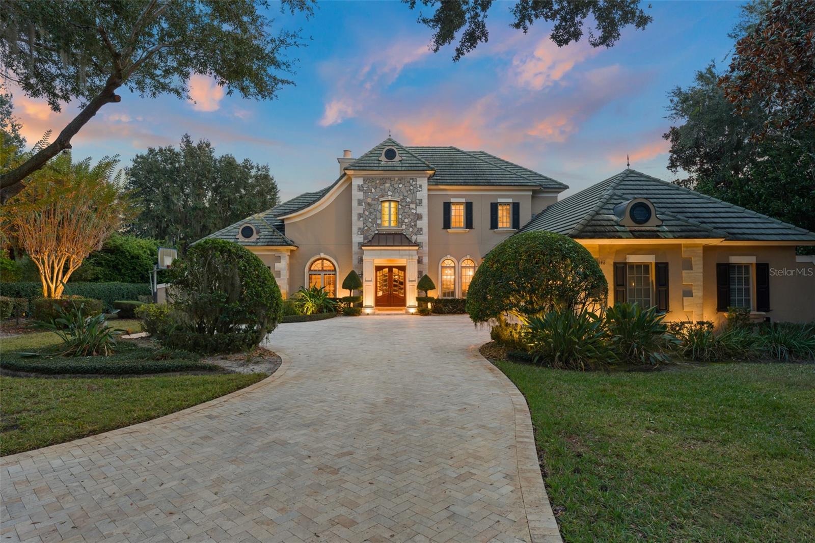 Nestled within the private gates of Isleworth West, a secluded enclave within the prestigious Isleworth community, this five-bedroom residence offers serenity and privacy against a backdrop of tranquil preserve views. Encompassing more than 6,200 square feet of thoughtfully designed living space, the home showcases elegant French country architectural styling, soaring volume ceilings, and exceptional custom finishes throughout. At the heart of the home, an inviting central gathering area seamlessly connects the center-island kitchen, casual dining space, and a warm, light-filled family room—ideal for both everyday living and effortless entertaining. The kitchen is appointed with custom light-toned cabinetry, granite countertops, and a full suite of Viking and Sub-Zero appliances, combining timeless design with exceptional functionality. Formal living and dining rooms provide graceful settings for more elevated occasions. The home office serves as a true standout, featuring a dramatic cathedral ceiling accented by exposed wood beams and richly crafted built-in cabinetry—an inspiring retreat for work or study. The expansive primary suite on the main level offers a serene escape complete with pool access, an expansive walk-in closet, and an elegant bath highlighted by exquisite dual vanities. Upstairs, a spacious bonus room currently configured as a home theater provides a versatile space for entertainment or relaxation, opening to a large balcony featuring picturesque views of the surrounding nature preserve. Designed to embrace Florida living, the screened and covered lanai features a summer kitchen and fireplace and opens effortlessly to a sparkling open-air pool and spa. Completing the residence is a three-car garage, offering ample space for vehicles and storage. An exceptional offering in one of Isleworth’s most private settings, this residence blends architectural character, refined interiors, and resort-style outdoor living in a truly distinguished environment.