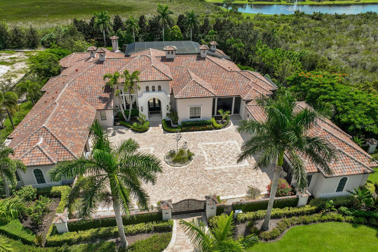 A true lifestyle estate in The Lake Club, built in 2015, offering unparalleled luxury and amenities—all on one level. This private, walled estate is nestled within the gated community of The Lake Club, surrounded by lush foliage and serene Savannah landscapes, creating the ultimate private oasis. Designed for both grand entertaining and everyday comfort, the home boasts exceptional features, including full house generator, Andersen impact windows, private tennis and basketball courts, putting green, motor courtyard, billiards and media room, library, and a 1,000-bottle wine chamber. The fully air-conditioned garage, and fitness area provide incredible flexibility and can be easily converted into additional living space. From the moment you step through the soaring 13-foot wrought-iron double doors, the 22-foot ceilings of the Grand  Parlor set the tone for the home's exquisite craftsmanship. Custom details abound, including Travertine and hardwood flooring, extensive granite, curved stone and coffered ceilings with exposed beams, and two hand-carved walnut fireplaces. The gourmet kitchen, designed to impress, opens to the gathering room and features a wraparound bar, large island, Wolf appliances, a Butler’s pantry, and a breakfast nook with a coffee station. The secluded Owner’s wing ensures maximum privacy, while four guest suites are thoughtfully placed on the opposite end of the home. Enter your personal sanctuary with this stunning master suite, where luxury harmonizes with comfort. This generously sized retreat is meticulously crafted for the perfect getaway, complete with a library, study, and private patio. The en-suite bathroom boasts a soaking tub, dual vanities, and a garden walk-in shower. The inviting sitting area encourages you to relish peaceful moments, while the spacious walk-in closet provides plenty of room for all your wardrobe essentials. Expansive walls of pocketing glass sliders seamlessly blend indoor and outdoor living, leading to the breathtaking brick-pavered lanai. Here, you'll find a 35-foot-high protected cage, cabana, summer kitchen and bar, outdoor fireplace, designer pool, and raised spa—all perfect for Florida’s year-round entertaining. Experience the pinnacle of luxury living in The Lake Club, where residents enjoy access to a wealth of amenities, including two resort-style heated pools, Grande Clubhouse with fine dining and bar area, a fitness center, spa, tennis courts, pickleball, a playground, dog park, and services of a full-time concierge and activities director.