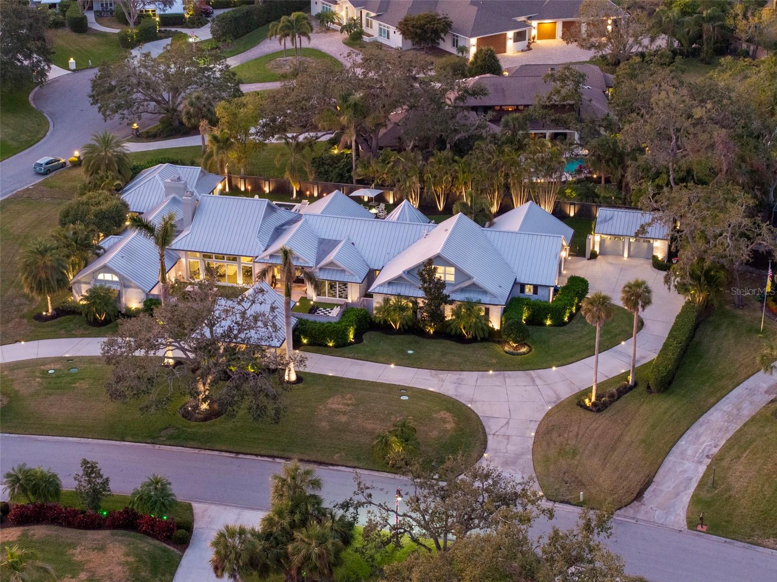 Nestled on nearly an acre within the prestigious gated community of Beneva Oaks, this masterfully designed 7,023 sf estate offers an unparalleled blend of luxury, thoughtfully appointed spaces, and architectural beauty. Positioned on an oversized corner lot, the home welcomes you with a stately porte-cochère and a charming walled front courtyard—perfect for al fresco dining or a private garden retreat. Upon entering the grand foyer, you are greeted by an open and flowing layout where expansive yet distinct indoor and outdoor living spaces are beautifully integrated. Vaulted wood-beamed ceilings enhance the sense of openness in the living areas, bedrooms, and office, while Karastan luxury flooring connects each room with elegance and warmth. Stunning Restoration Hardware chandeliers and eye-catching wallpaper from Belgium’s renowned Omexco Group add striking texture and depth to key spaces, further elevating the home’s refined aesthetic. The combined living room and dining area is framed by a wall of pocketing sliding glass doors on two sides, filling the space with light and offering picturesque views of the backyard with sparkling pool and the charming front courtyard. A striking oversized Italian porcelain tile wood-burning fireplace serves as the focal point which adds a bold statement of modern sophistication. Adjacent to this space is the opulent primary suite, which rivals the finest five-star hotels. Soaring vaulted ceilings create an atmosphere of grandeur. Glass doors open to the patio and pool, and a circular walkway leads you to a large walk-in closet, dressing room, and sumptuous bathroom retreat complete with oversized spa tub and spectacular walk-in shower. The welcoming family room boasts an electric fireplace and wall of sliders that seamlessly blend indoor and outdoor spaces. The kitchen is a masterpiece of elevated design, featuring an octagonal breakfast nook with bay windows and a show-stopping island with 2.5" Luxury Series Cambria quartz countertop in a design-forward tiger-stripe pattern and matching hood. Custom cabinetry in a mix of dark and white finishes and metallic accents round out the dramatic fusion of this bold yet harmonious culinary space. Three generous bedrooms with en-suite baths, large office, craft/mudroom with island, laundry room with dog-washing station, and abundant storage round out the main level. Upstairs is the spacious 5th bedroom currently used as a bonus room with additional storage space. The expansive backyard is designed for grand-scale entertaining, featuring a large, covered seating area overlooking the saltwater pool and spa, ample green space, putting green, and fully-equipped and covered summer kitchen with an island, refrigerator, dishwasher, and rotisserie grill. A private gym completes this resort-style outdoor retreat. Meticulously designed by award-winning interior designer Leila Fatemi, most of the home’s finishing touches are sourced from Global Views, creating a flawless blend of luxury and artistry. Every detail of this home has been thoughtfully curated, with hand-selected designer furnishings, available for purchase on a separate bill of sale. Close proximity to Sarasota's dining, shopping, culture, & the pristine Gulf of Mexico beaches, this exceptional property offers an unparalleled combination of design, craftsmanship, and opulence in one of Sarasota’s best-kept secret neighborhoods, presenting a rare opportunity to experience refined Florida living at its finest!