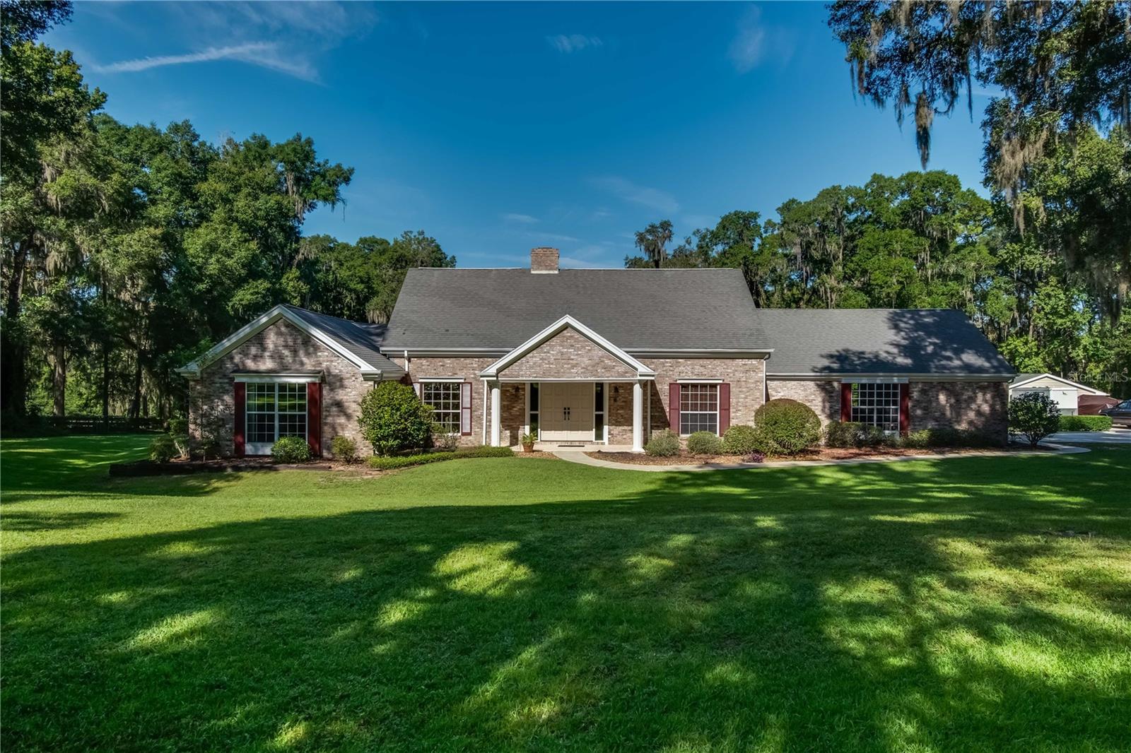 Nestled on a quiet stretch within the neighborhood of Shady Road Ranches, this stunning estate offers the perfect combination of private, picturesque, and convenient! Fenced and gated, the property has a picturesque setting and lots of curb appeal with just under 5-acres of gently shaded countryside adorned with professional landscaping. At the heart of the estate is the stunning 3-bedroom, 3-bath multi-story home. The first floor features the main spaces of the home, offering high ceilings, lots of natural light, and a spacious layout. A cozy fireplace serves as the focal point in the primary living area, making it the perfect place to relax on cooler winter nights. For those who enjoy cooking, the kitchen is well appointed– there is abundant cabinet and counter space, stainless steel appliances, tiled backsplash, under-cabinet lighting, and a large center island. Another unique feature in the kitchen is the pass-through window that directly connects to the Sun Room– a wonderful option that makes hosting a true breeze. The formal dining area is directly  connected to the living area and features lovely built-in shelving units with plenty of space for displaying collectibles, books, photos, and everything in between. The master suite is also located on the first floor, offering a stunning retreat that features a huge layout that includes a hallway with built-in shelving units, a private seating area with fireplace, a huge walk-in closet with shelving, and private en-suite with linen closet, large vanity, a large tub, and glass-door shower. If hosting is a passion, the back of the home is a perfect oasis to take advantage of. Outfitted with huge windows and ample space, the Sun Room is air conditioned and provides a built-in wet bar, entertainment area with TV, lots of space for seating, and ceiling fans to keep things cool. A pair of french doors open up to the expansive pool deck which surrounds the sparkling in-ground pool with diving board, all overlooked by an upper balcony with an exterior spiral staircase. Beyond is a huge backyard that has been meticulously maintained and landscaped. On the second floor are the remaining bedrooms and a shared bathroom. Both bedrooms feature direct access to the expansive second floor balcony, which directly overlooks the backyard and pool area, as well as attic access. Beyond the main home is a private studio-style apartment, which could be used for guest accommodations, in-laws, or even as a separate entertaining space or office if desired. Fully equipped with its own kitchen, a full bath, and ample space, there is tons of flexibility to how this space could be used! This property is located just minutes from the Florida Horse Park and a short drive from Ocala’s variety of shopping, dining, entertainment, and medical options, giving it the perfect blend of quiet and convenient! A must-see property that shouldn’t be overlooked, this charming estate is a true Ocala gem!
