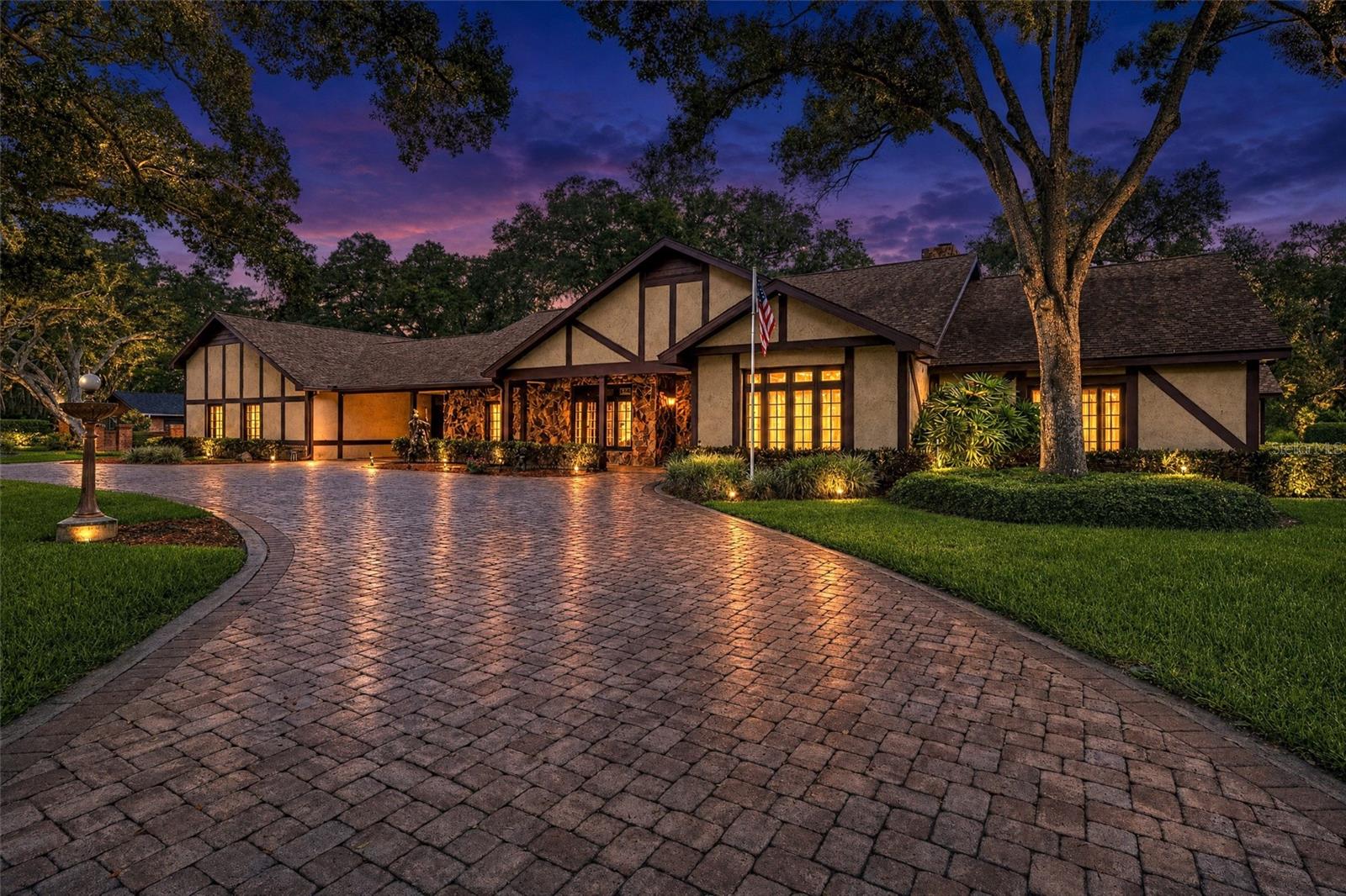 Tucked away on a sprawling, oak-canopied lot of nearly an acre, this stately residence in Clearwater's highly sought-after Wedgewood Estates offers an unparalleled blend of architectural character, generous scale, and resort-style outdoor living. Boasting over 6,100 square feet of heated living space, this remarkable home is designed for both grand-scale entertaining and comfortable everyday living, surrounded by the tranquility of mature landscaping and beautiful grounds. A sweeping circular paver driveway leads to a striking Tudor-inspired facade, framed by magnificent shade trees and dramatic landscape lighting that creates an unforgettable evening presence. A covered drive-through breezeway connects the residence to the garage wing, creating a striking architectural feature while providing sheltered access and additional covered parking. Complementing the estate's functionality is a substantial pavered motor court behind the garage, offering abundant space for RV and boat parking, collector vehicles, and large-scale guest accommodations. Upgrades include a Full House Generator (2019), Two Tankless Hot Water Heaters (2019), New Flat Roof (2025), a Beautifully Remodeled Kitchen, Deep Well for Irrigation, and much more! Step through the double glass entry doors into a grand foyer that sets the tone for the home's impressive interiors. This home features 6 Bedrooms, 5 Bathrooms, an Executive Office with Private Entrance, a 1-Bedroom Apartment, a Large Bonus Room with Pool Bath, an open gym/rec area, an Open Loft, Storage Rooms, and much more! The flowing floor plan effortlessly connects formal and casual spaces, featuring a chandelier-lit dining room and an expansive family room anchored by a dramatic stone fireplace wall and highlighted by rich wood-beamed ceilings that add warmth and architectural character. Wide-format tile flooring, rich wood accents, and custom stained-glass details add warmth and timeless elegance throughout. The heart of the home is a spacious, open-concept kitchen featuring granite countertops, custom wood cabinetry, a tile backsplash, and an inviting layout that overlooks the main living areas. This home offers tremendous flexibility for a buyer to enjoy its classic charm or further customize and modernize the spaces to their exact vision. What truly sets this property apart is the combination of two extraordinary bonus spaces that most homes of any size simply cannot offer. A large, dedicated home office features its own private entrance and a full bathroom, making it ideal for a home-based professional, a creative studio, or a private guest suite entirely separate from the main living areas. In addition, a fully detached in-law suite offers complete independence with a private one-bedroom layout, a full kitchen, and a full bathroom. Whether accommodating extended family, hosting long-term guests, or generating rental income, the possibilities are endless. 
Step outside to discover a private, resort-inspired oasis. The massive screen-enclosed pool area is a true showstopper, complete with a custom rock waterfall and slide feature that promises endless entertainment. Broad paver decking provides abundant space for entertaining, all while overlooking the expansive, lushly landscaped backyard.
Located in a premier Clearwater neighborhood with no flood insurance required (Zone X), this estate delivers the ultimate combination of privacy, space, and lifestyle versatility.