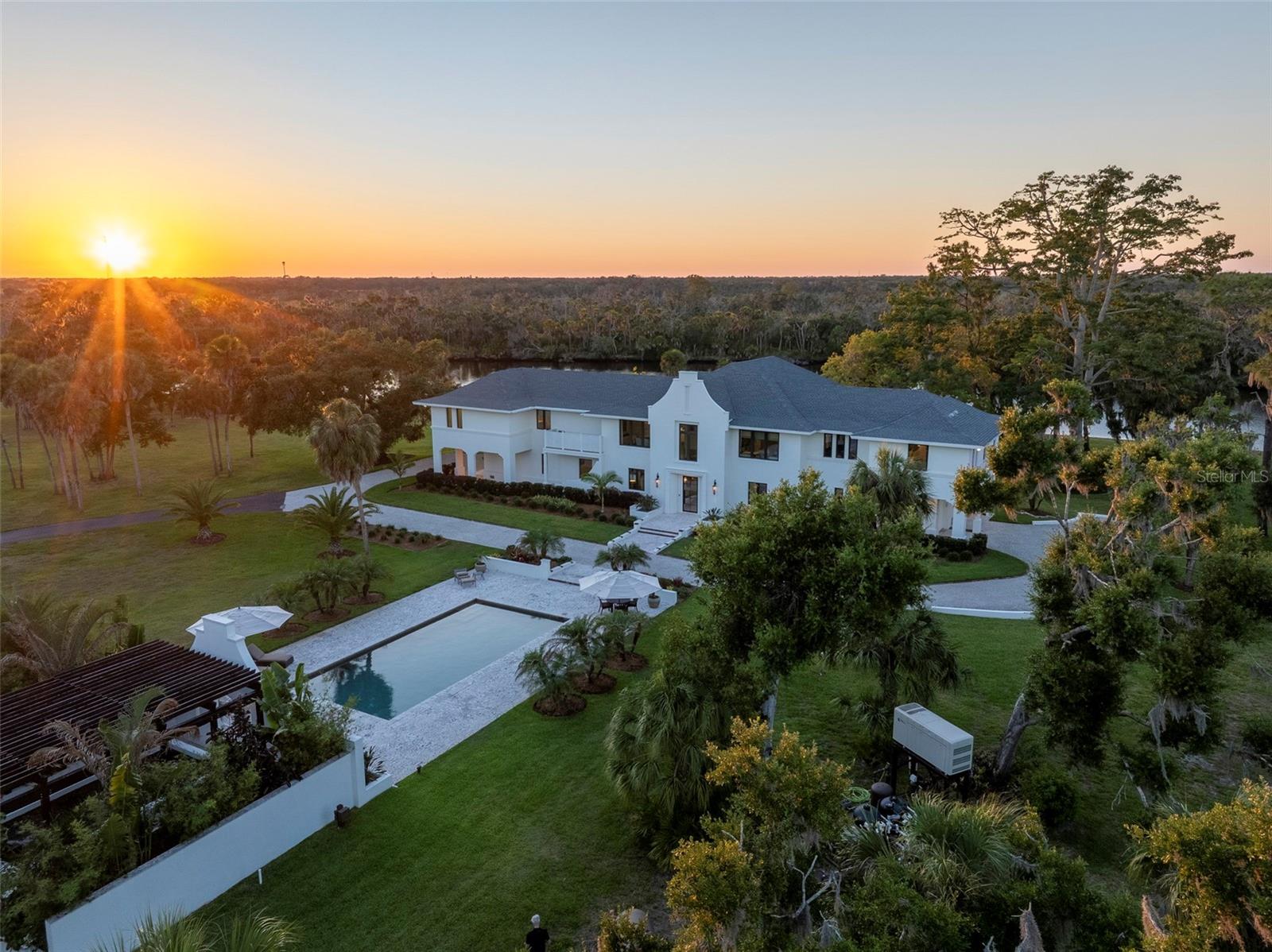 Tucked away along the tranquil banks of the Manatee River, this extraordinary 30-acre private estate offers a lifestyle rarely found in Sarasota or Manatee County—where outdoor adventure, recreation, privacy, and luxury converge into one remarkable compound. The property features an exceptional 4,489 sf custom home built in 2021, a 1,282 sf guest house, a multi-use air-conditioned outbuilding and more, and offers a true Florida playground for boating, fishing, horses, entertaining, hobbies, and enjoying the outdoors on an unmatched scale. A 60-foot dock provides direct access to incredible fishing and boating, with tarpon, snook, redfish, black drum, blue crab, dolphin, and manatee, all part of everyday life along this serene stretch of river. Explore the estate through an extensive network of raised walking and ATV trails winding beneath majestic moss-draped oaks and along the water’s edge, leading to hidden gathering spaces, multiple firepit areas, sunset overlooks, and a screened riverfront “Fish Shack” complete with a sink for cleaning the day’s catch after time on the water. Agriculturally zoned and exceptionally versatile, the property allows horses, farming, honey beehives, recreational vehicles, and even the installation of a helipad. Expansive open land provides endless possibilities for sporting activities, additional structures, or simply enjoying unmatched privacy surrounded by nature. The spectacular main home offers a flexible open-concept floor plan and showcases natural materials including coral stone, shellstone, quartzite, and rich acacia wood. The well-designed space includes two spacious bedroom suites, 3rd bedroom/study, living and dining rooms, media/family room, Chef's kitchen, office, gallery, mud room, gym, hobby room, and elevator. Stunning views from every room, and covered terraces and outdoor gathering spaces extend the living experience outdoors. The separate elevated 1 bedroom/1 bath guest house built in 2020 known as “The Treehouse" features a spacious living room and bedroom, with dramatic oversized windows overlooking a peaceful pond. The massive 60’ x 30’ air-conditioned and insulated multi-use outbuilding/barn with office and full bath is ideal for car collections, boat or RV storage, horses, woodworking, fitness training, sports simulation, hobbies, or additional entertaining space. Total garage space for 15+ cars/RVs/boats! A stunning heated resort-style saltwater pool, beautiful koi pond, greenhouse with nursery system, wetland island, tropical landscaping, and abundant wildlife create a setting that feels worlds away from city life in a location that is remarkably convenient, just minutes to I-75, approximately 15 minutes to shopping and dining, and 30 minutes to Sarasota-Bradenton International Airport. Rarely does a property combine this level of privacy, acreage, architectural quality, and outdoor lifestyle in such a convenient Sarasota-area location. This is a once-in-a-generation opportunity to own a true legacy property where the Florida outdoor lifestyle can be lived to its fullest.