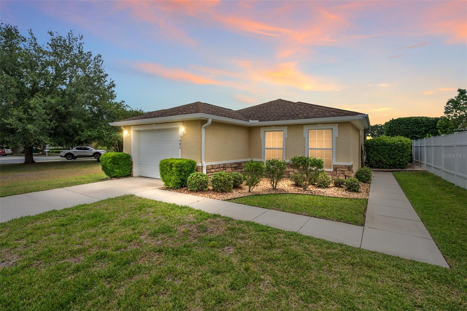TAKE A CLOSE LOOK at this MOVE-IN READY HIDDEN GEM with NO HOMES BEHIND in the GATED, family-friendly community of THE VILLAGES OF PARKWOOD in Oxford, FL! This well maintained 2 BR / 2 BA / 1 Car Garage home with 1,221 SF of living area delivers a wonderful blend of comfort, convenience, rear privacy, and community amenities at an approachable monthly HOA fee of $85. Perfectly situated in the BRENTWOOD section of Parkwood on an OVERSIZED ~0.14 acre lot, this home is just a short ride to the CR 466 COMMERCIAL CORRIDOR for shopping, dining, medical, banking, & services. You will also be just around the corner from the Parkwood community recreation center and only about 7 minutes / 1.8 miles from the highly ranked Villages Charter School! Curb appeal makes a great first impression with a CONCRETE BLOCK & STUCCO exterior, partial STONE VENEER accent on the front elevation, refreshed front landscaping, and a concrete walkway that wraps around to a very private COVERED SIDE ENTRANCE. The oversized lot provides valuable ROOM TO EXPAND on the east side of the home—whether you envision an outdoor haven, expanded patio space, garden area, or simply extra breathing room to enjoy. Step inside and you will appreciate the inviting OPEN CONCEPT, SPLIT BEDROOM FLOOR PLAN with VOLUME CEILING (~9 ft) over the main living area. The combo LIVING/DINING ROOM feels welcoming with HAND-SCRAPED ENGINEERED WALNUT HARDWOOD FLOORING, a TRAY CEILING over the DINING ROOM, and SLIDING GLASS DOORS leading to the SCREEN-ENCLOSED LANAI. The KITCHEN is functional w/ adequate countertop space, featuring OAK WOOD CABINETS, BEVELED EDGE laminate countertops, a pony BREAKFAST BAR for casual seating, and updates including new REFRIGERATOR (2024) and STAINLESS STEEL SINK. The guest side of the home is smartly arranged with a hallway LINEN CLOSET, entrance to BEDROOM 2, garage access, and an INDOOR LAUNDRY space tucked neatly behind bifold closet doors. BATHROOM 2 features a deep TUB/SHOWER COMBO with TILE SURROUND, COMFORT HEIGHT TOILET, and single vanity with BEVELED EDGE countertop. On the opposite side of the home, the spacious PRIMARY BEDROOM offers a TRAY CEILING, large closet with bifold doors, and its own SLIDING GLASS DOORS to the lanai. The ENSUITE PRIMARY BATHROOM provides DUAL SINKS in a double vanity with BEVELED EDGE laminate countertop, plus a private, separately enclosed area with a tiled WALK-IN SHOWER and COMFORT HEIGHT TOILET—an excellent layout for simultaneous two-person use of the bathroom space. The SCREEN-ENCLOSED LANAI is a peaceful place to relax with morning coffee, unwind after a busy day, or enjoy the privacy created by having NO HOMES BEHIND. Additional practical features include: ARCHITECTURAL SHINGLE ROOF (2009), HVAC (2022), HWH w/ thermal expansion tank (2024), HALO whole house water filtration system (2024), new garage door opener, and Hunter irrigation system with new control panel (2022). Parkwood residents enjoy access to a community recreation center with fitness center and resort-style swimming pool, tennis court, basketball court, and playground, creating a convenient neighborhood setting for active everyday living. With rear privacy, move-in ready appeal, an oversized lot, community amenities, and a fantastic location near CR 466 conveniences, this special home is one you will not want to miss. Schedule your private showing today! NOTE: Parkwood is an independent community NOT affiliated w/ The Villages®, a premier 55+ community.
