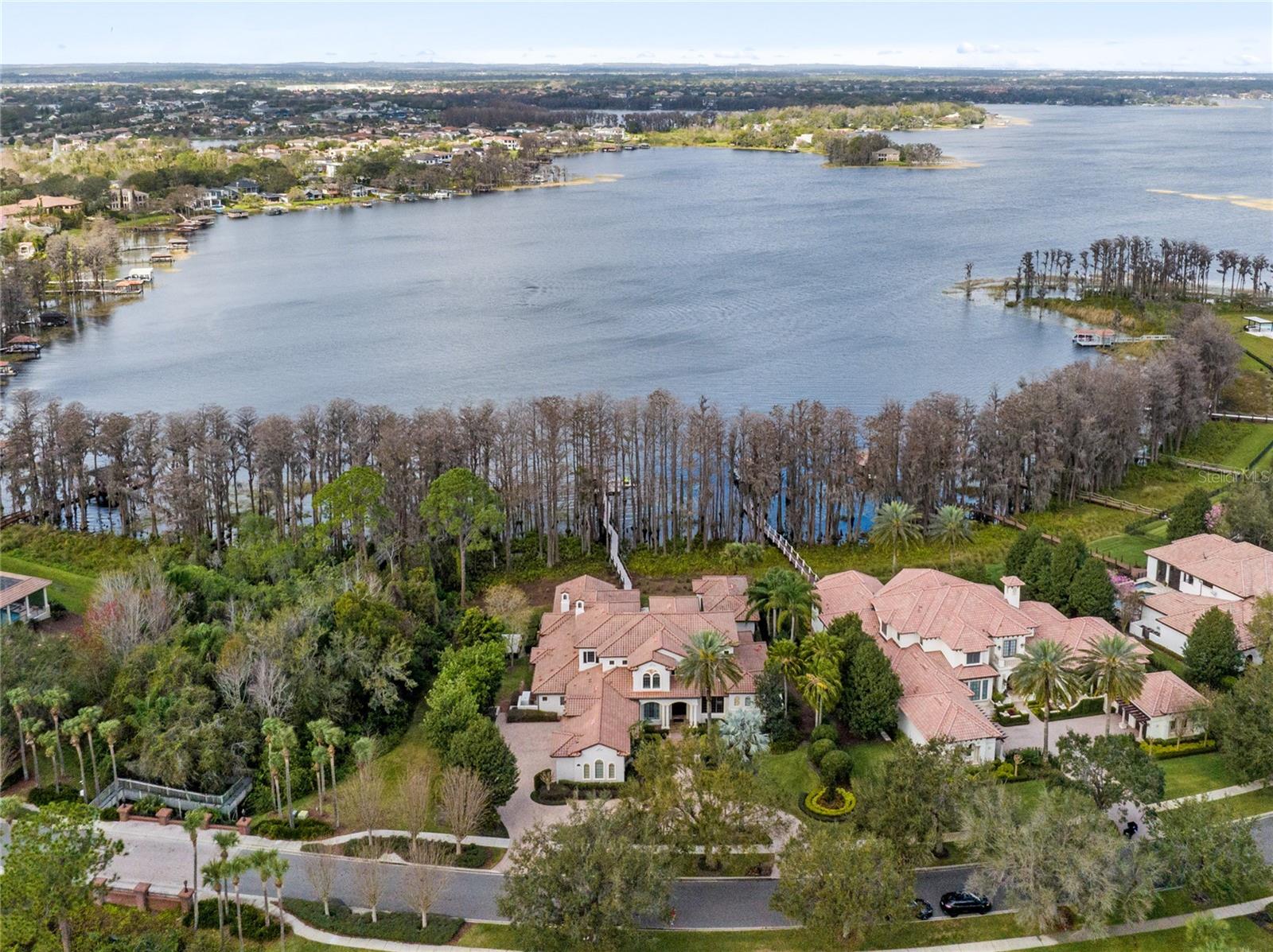 A home designed for entertaining and intimate gatherings focused on comfort, convenience, and functionality. Welcome to the guarded gated community of Reserve at Lake Butler Sound on the Butler Chain of Lakes. Extensive renovations in 2021 resulted in a beautiful and functional living space offering 6 bedrooms, 7.5 baths, an infinity edge pool, & cabana house with a full bath & requirements to create the recreation space or a separate bedroom suite. Rustic Spanish Mediterranean mahogany front doors open to 24' ceilings in the foyer with an exceptional pool & lake view. The living room boasts identical ceilings & views, with a cozy fireplace, perfect for relaxing with loved ones. Gorgeous 36" marble flooring spans from the foyer & formal areas into the kitchen, family room, and down the glass corridor. The bonus & game rooms, lofts, executive office, & all bedrooms offer new wood flooring. The formal dining area & spectacular new lighting are the ideal accompaniment for the redesigned fashionable chef's kitchen. New marble counters, a redesigned farmhouse island, stylish cabinetry, & top-of-the-line Viking & Sub-Zero appliances view the family room & dinette with restored beams. Large windows provide abundant natural light highlighting 12ft ceilings, a fireplace, and the perfect space for a Grand Steinway. Behind the kitchen is the brand-new modern-contemporary-designed frameless glass wine cellar showcasing your collection. Nearby is the bonus room, two bedrooms with ensuites, and a laundry area with a new second dishwasher, apart from the outdoor side-screened room with a fireplace. The first-floor owner's suite features a gorgeous view, an enormous spa-inspired private bath with a soaking tub & oversized shower, and a two-story closet with a center island, comfortable lighting, and ample space. An adjacent custom-built executive office with fine hardwood built-ins provides the perfect working environment. The second floor has a dedicated theater room with great sound, a massive projection system, and remote blackout blinds. The redesigned game room features a new bar, appliances, built-ins, and access to a grand veranda with a view of the resurfaced pool, patios, cabana, and the chain of lakes. You will also find two more bedrooms with full baths—one with plantation shutters and the other with remote blinds & access to the veranda. Between the floors is a unique kid's area with a loft. It's the perfect spot for play and creating new memories. Open the eight side-by-side French doors to the covered patio & BBQ kitchen with two wine refrigerators, ice maker, and a wet bar. Expand your entertaining outdoors, creating perfect summer barbecues, special occasions, and significant holiday events. The cabana house is ideal for guests or your private getaway, featuring new wood flooring, gas fireplace, & a remodeled full bath. Walk down the 200ft eco-friendly pathway leading to a 26x27 boat dock made of composite wood. The boat dock has a power lift and sensational views. Additional features include a basketball court, multiple fireplaces, a 4-bay side entry garage, 2 New HVACs, a New water heater, New dishwashers, wood ceilings, plantation shutters, remote blinds, & a Brand New Generac 60W natural gas generator providing power to the entire home power when needed. Historic downtown Windermere, Dr. Phillips, and the 408/429/Turnpike grant access to New hospitals, Disney World, OIA, and Central Florida.