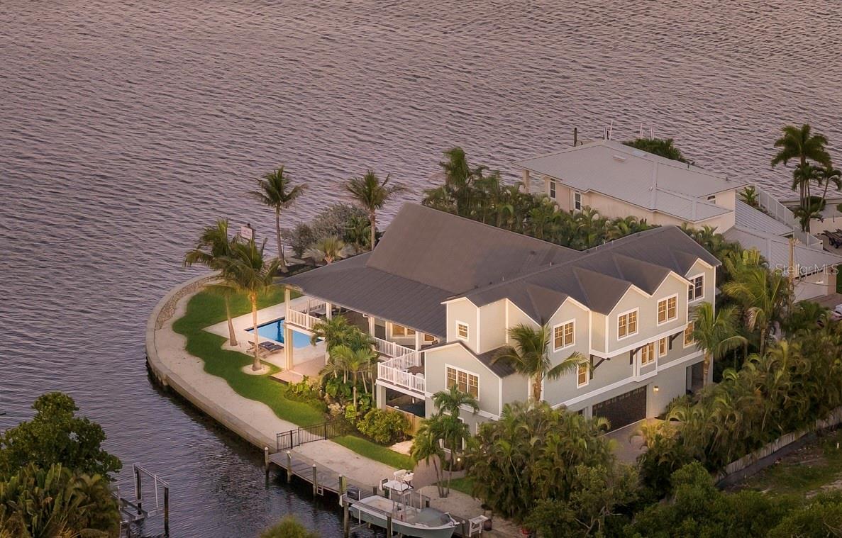 Tucked along an extraordinary 225 feet of waterfront, this custom coastal retreat distills the very essence of island living—breathtaking water views, exceptional privacy, and thoughtfully designed spaces that move effortlessly between serene relaxation and spirited entertaining. A palm-lined driveway sets the tone, where timeless architecture and lush tropical landscaping leave an unforgettable first impression.
This residence carries rare local significance as the very first custom home built by Ross Built Construction, masterfully designed by renowned architect Gene Aubry. It stands as a lasting testament to their craftsmanship and creativity—and their contribution to luxury coastal living on Anna Maria Island. Their influence resonates throughout: a thoughtful floor plan, an exceptional command of natural light, and a seamless connection between indoor and outdoor living.
Inside, travertine tile and hand-scraped maple flooring flow through a light-filled interior crowned by soaring vaulted ceilings in the living and kitchen areas. The chef's kitchen is as functional as it is beautiful, appointed with stone countertops, copper sinks, a gas range with pot filler, premium appliances, and a generous center island that anchors the home's main gathering spaces.
Five spacious ensuite bedrooms, a dedicated den/office, and an upstairs bonus room offer effortless flexibility for family and guests. The primary suite is a private sanctuary unto itself, featuring a remodeled spa-inspired bath with custom built-in shelving and elegant finishes throughout.
Designed to embrace the waterfront lifestyle, expansive glass doors open to an impressive 1,400-square-foot veranda overlooking the sparkling saltwater pool and tranquil waterways beyond. Boaters will appreciate the private dock and 10,000-lb boat lift for effortless access to open water, while an oversized three-car garage, elevator, impact-rated windows and doors, Sonos sound system, mosquito misting system, rainwater cistern, and exterior irrigation system deliver convenience and lasting peace of mind.
Perfectly positioned in the heart of Holmes Beach, the property is just moments from the sugar-sand beaches of the Gulf, beloved local restaurants, boutiques, and island shops—a rare pairing of private waterfront sanctuary and walkable island convenience. Whether savoring spectacular sunsets from the veranda, entertaining poolside, strolling to nearby dining, or setting out for a day on the water, this remarkable residence offers something exceedingly rare: not only an extraordinary waterfront home, but a meaningful piece of island history, where inspired architecture, enduring craftsmanship, and an unrivaled setting come together in perfect harmony.