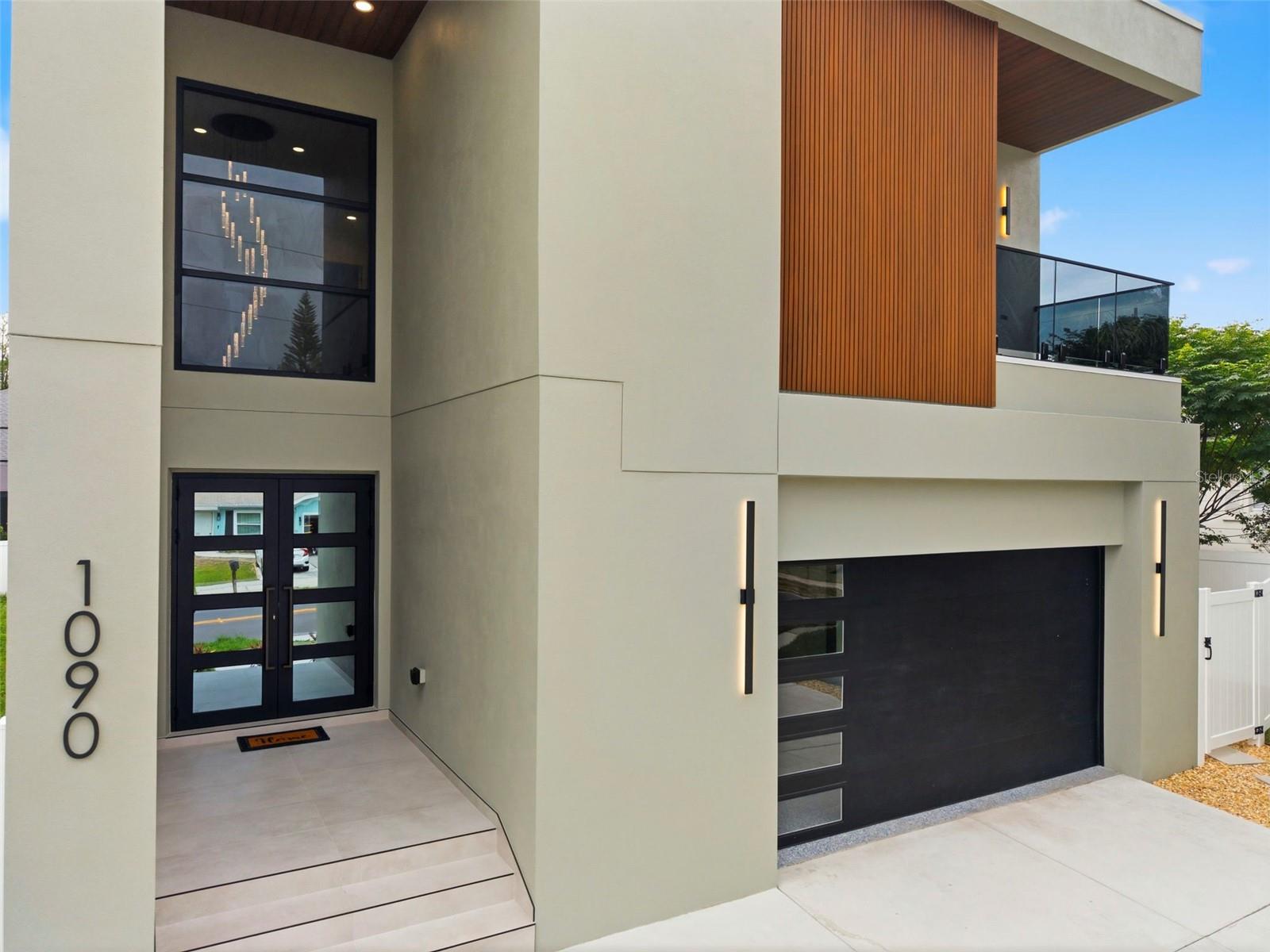 Stunning new construction mid-century modern two-story home located on highly sought-after Main Street in Safety Harbor. Designed with elevated finishes and modern architectural elements throughout, this impressive residence features a torch-down flat roof, double driveway with turnaround pad or golf cart parking, and a private vinyl-fenced backyard with gates on both sides. Outdoor living spaces include a covered lanai and second-floor balconies at both the front and rear of the home.

Enter through double doors into a dramatic foyer with soaring 20+ foot ceilings highlighted by a modern crystal sloping pendant chandelier. The foyer also provides direct access to the oversized two-car garage. The open-concept floor plan seamlessly combines the living room, kitchen, and dining areas, showcasing layered textures of stone, wood, and Venetian plaster throughout the home. Thoughtful design details maximize storage and functionality.

The living room features custom built-in wood shelving and an electric decorative fireplace. Designed for entertaining, the kitchen opens directly to the backyard and lanai through sliding glass doors and offers dual-tone cabinetry, granite countertops, an island with an extending sliding countertop for additional seating and storage, and premium European-style FORNO Espresso appliances. The elongated dining area runs parallel to the kitchen, creating a spacious and inviting gathering space.

Additional first-floor features include a small pantry connected to the half bathroom, a versatile flex room ideal for an office, den, or library, and a glass-enclosed wine display and storage area beneath the staircase.

Upstairs, the second-floor landing overlooks the foyer with modern glass railings and connects all bedrooms along with the upper-level laundry room. Every bedroom includes ceiling fans, window treatments, ensuite bathrooms, and generous closet space.

The spacious primary suite features sliding glass doors leading to a private rear balcony, a dry bar, walk-in closet with built-ins and vanity, and a luxurious ensuite bathroom with dual sinks, a walk-in glass shower with rain shower head, and a contemporary freestanding soaking tub. Secondary bedrooms offer ensuite bathrooms with single vanities and glass-enclosed tub/shower combinations. The front bedroom also enjoys access to a private balcony overlooking the property.

The upstairs laundry and storage room includes cabinetry, countertop workspace, sink, and washer/dryer hookups for added convenience.

Conveniently situated on Main Street with quick access to McMullen Booth Road/County Road 611 and less than one mile from downtown Safety Harbor, this home offers the perfect balance of luxury and location. Nestled along the western shore of Tampa Bay, Safety Harbor is known for its charming small-town atmosphere, waterfront parks, renowned resort and spa, locally owned shops and restaurants, community events, recreational activities, and beautiful Philippe Park.