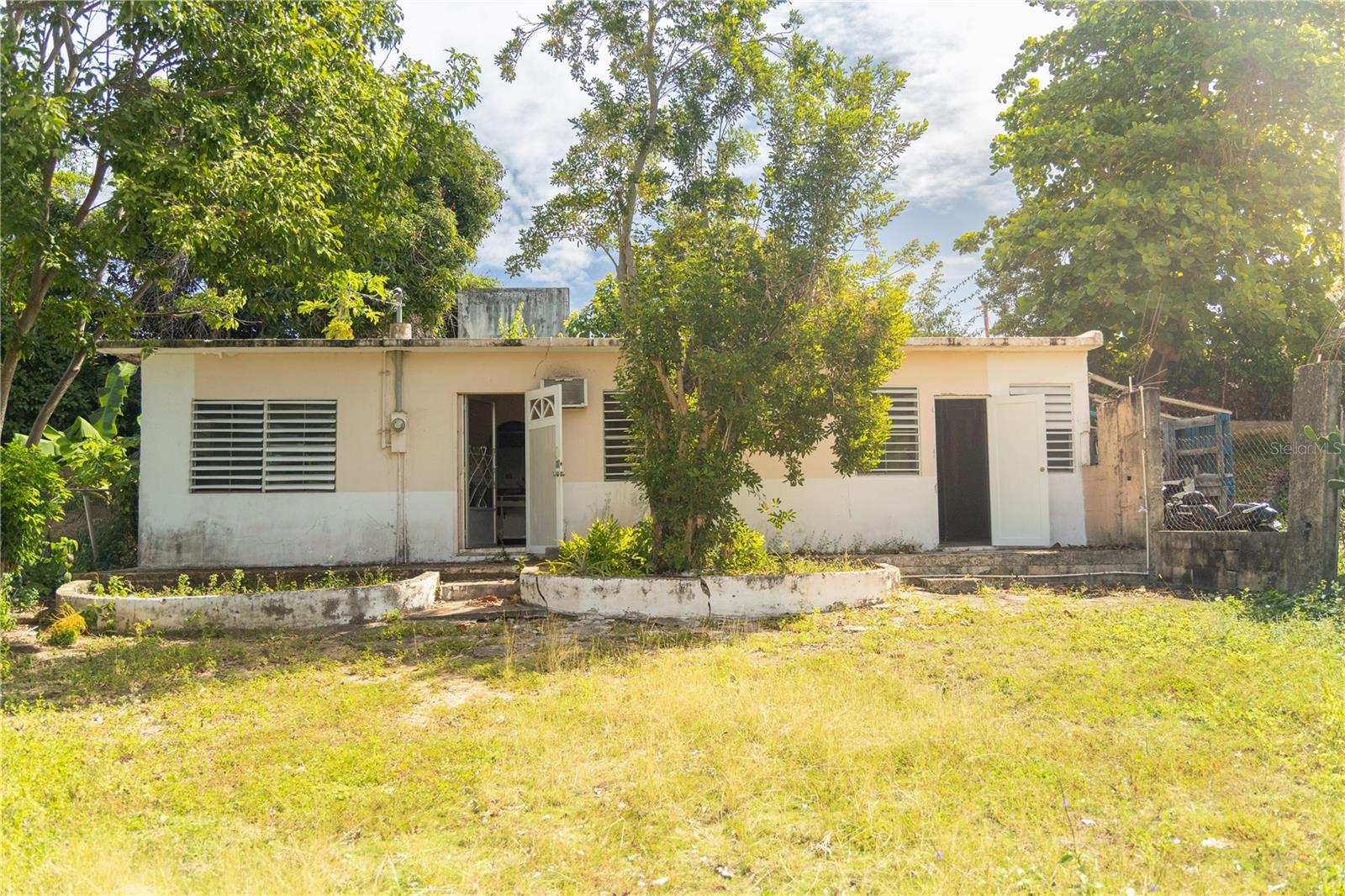 This two bedroom, one bath home in the peaceful neighborhood of Las Marías, presents a wonderful opportunity to create your ideal island home. Located mid-island in Vieques, you’ll enjoy convenient access to key amenities including the supermarket, gas stations, town, post office, and restaurants.

Set toward the back of the property, the home feels bright, quiet, and removed from the street. Inside, you’ll find a bright and inviting living room that flows into a comfortably sized kitchen. Just off the kitchen is a dedicated laundry area for added convenience. The main house features a spacious bedroom and a full bathroom.

A standout feature of the property is the separate room with its own private entrance, that can easily be closed off from the main home. The space is perfect for converting into a studio or guest suite, offering flexibility for a variety of living arrangements.

Outside, the property offers abundant potential. A welcoming front porch with decorative planters could be enhanced with an overhang to create a relaxing spot overlooking a future garden. The generous front patio provides ample space for off-street parking, landscaping, or even the addition of a pool. In the back, there’s room to cultivate a thriving vegetable and herb garden.

With good bones and plenty of opportunity to update and personalize, this property is is primed for renovation, whether you’re seeking a full-time residence, vacation getaway, or investment property.