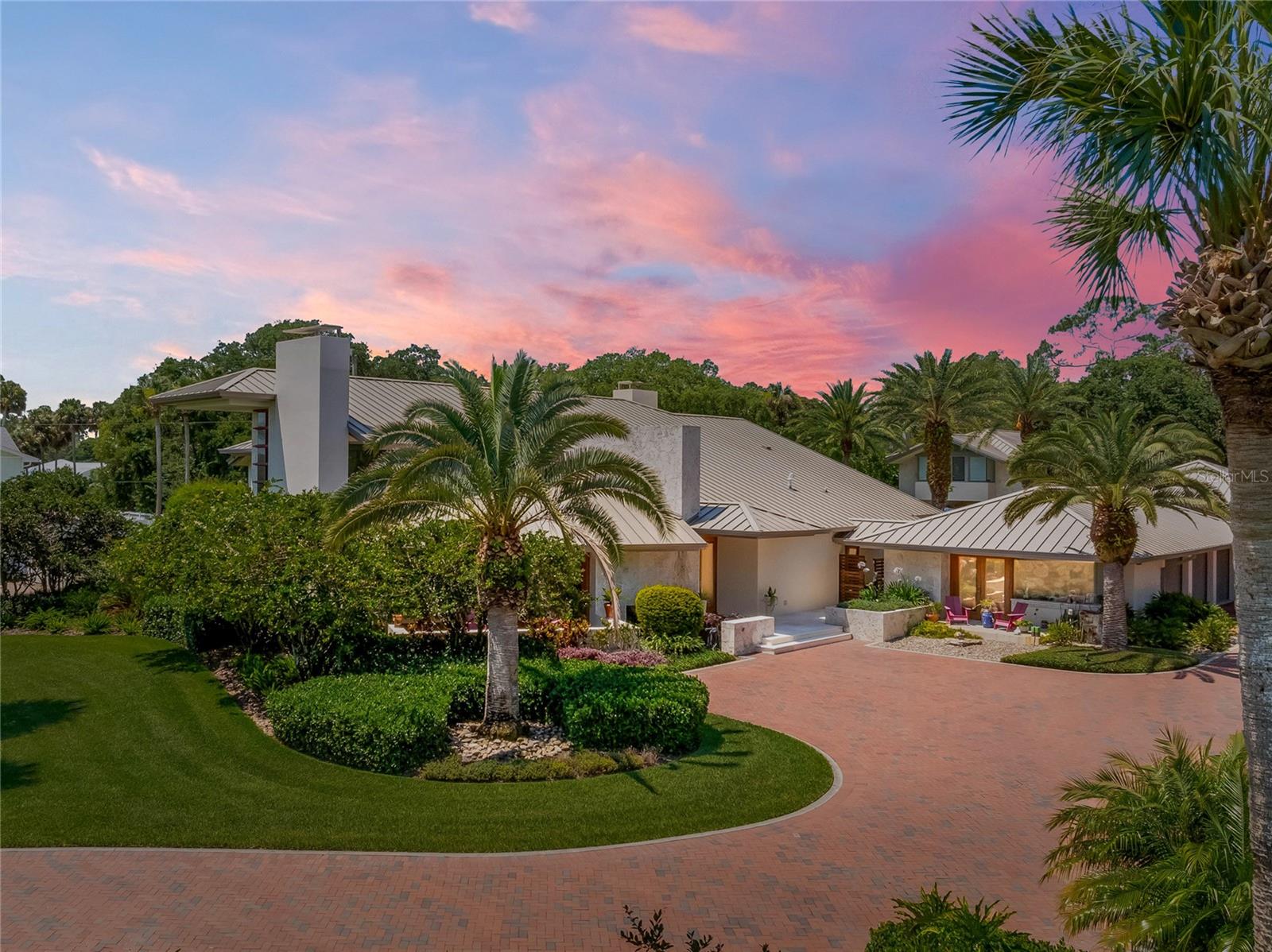 Nestled between the charming cities of Edgewater and New Smyrna Beach, this artist's dream home is a masterpiece of creativity, elegance, and functionality. Original owners and custom-designed by renowned architect Will Miller, this property exudes an eclectic and well-thought-out design, making it an ideal sanctuary for those with a passion for unique and inspiring living spaces. This family compound comprises three buildings: the main house (4455 sq ft), a guest/mother-in-law house (818 sq ft), and an industrial workshop(1200 sq ft) plus 2 separate garages and a separate art studio (286 sq ft). Spanning a generous 1.2-acre lot, the property is fenced and features a pavered driveway leading to the first three-car attached garage. Adjacent to the garage is an air conditioned art studio with large windows and beautiful views that allow bright light and a peaceful and creative environment to work in. Additionally, there is a separate 544 sq. ft cargo bay garage with a loading dock and 16” ceilings, attached to an oversized industrial workshop/man cave that comes equipped with a plethora of tools and machinery plus a 130 sq. ft loft/office space and half bath. Additional features include an Entire home Generator plus a 360 degree Video Surveillance system. The exterior has custom Florida Keystone thru out. The inside is an entertainer's dream with a complete open-concept layout.  Custom mahogany accents thru out. The first floor hosts a master retreat with a large bedroom on one side that connects to a luxurious master bathroom that includes a stand-alone bath tub, a spacious lit vanity with dual sinks, a shower with rain heads, a separate toilet and bidet, and access to an outdoor sitting area with a private shower, leading to the pool and spa. The master suite also features custom his-and-her closets with ample storage space to fit every need. Upstairs, two bedrooms each have their own personal bathrooms and balconies, offering stunning views of the Intracoastal Waterway and the pool. The open plan of this home boasts soaring ceilings, 24-inch limestone flooring throughout, a gas fireplace expanding to the ceiling, a sunken cozy living room, a family room, a dining room, an office space, and a temperature controlled wine cellar. The chef's kitchen is designed for culinary excellence, featuring high-end stainless and gas appliances- including Wolf and Bosch, a drop-down open concept, lighted stairs, a TV, and a built-in desk station. Adjacent to the kitchen is a butler's pantry or second kitchen, complete with a large serving area, another oven, dishwasher, ice maker, storage, and wine cooler, leading to a laundry room closet. The detached guest house comprises one bedroom, one full bathroom, a kitchen, and a living room. It features soaring ceilings, stone walls, and is handicap-friendly. Outside, the property transforms into a luxurious sanctuary with a covered patio, custom seating, a resort-style private salt water pool and spa, summer kitchen, a fire-pit, and more. Living here means enjoying a lifestyle that feels like a permanent vacation, with every inch of the home reflecting custom creativity and thoughtful design. Minutes to the boat ramp and beach. Short drive to Flagler Avenue and Canal Street. Embrace this vibrant community offering a perfect blend of relaxation and adventure before it’s gone. Be sure to watch the full VIDEO TOUR here : https://youtu.be/1OtTgaGE3Fo