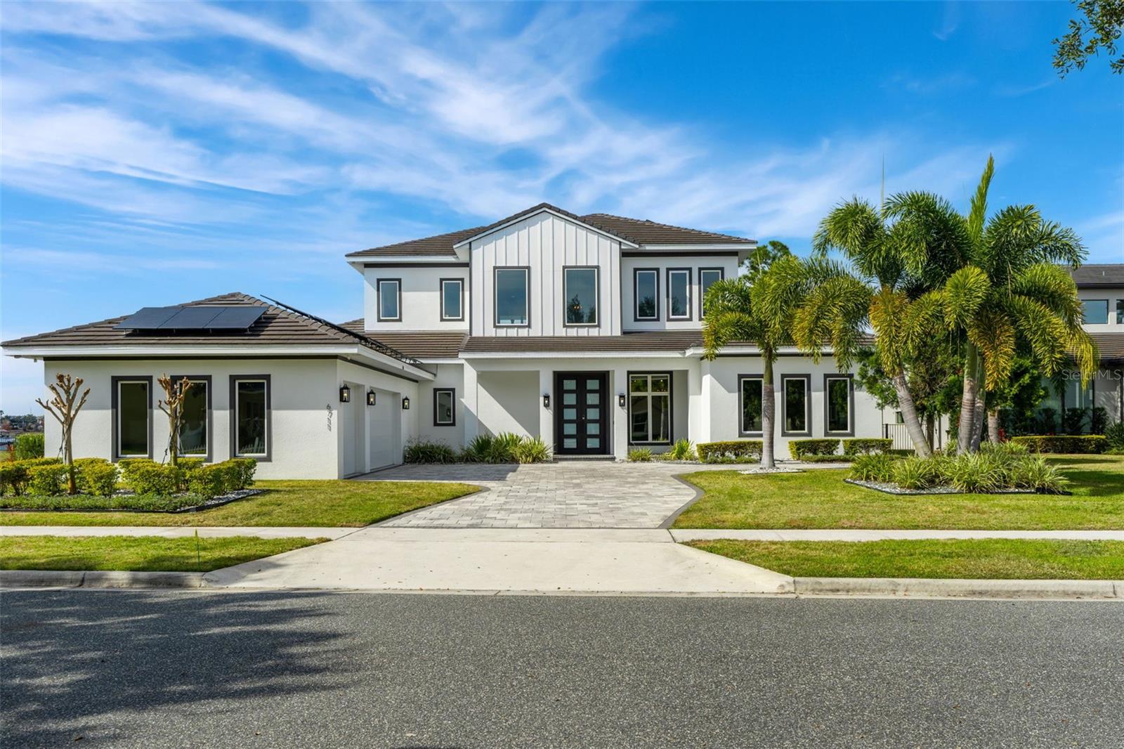 One or more photo(s) has been virtually staged. Welcome to this custom-built modern lakefront home by Davila Homes, located in Horizon West, Winter Garden, offering 5,433 square feet of living space with 5 bedrooms, 4 full bathrooms, and 2 half bathrooms, and direct frontage on Lake Hancock with approximately 85+ feet of shoreline and sunset views. Located directly across the lake from Hamlin Town Center, this 2021-built residence blends contemporary design and true waterfront living. A large driveway leads to the striking exterior, featuring a side-entry three-car garage and a dedicated home office with a private exterior entrance. Upon entering through the double front doors, soaring ceilings and open sightlines immediately reveal pool and lake views. The main living areas are designed for open-concept living and entertaining, featuring 2x4 porcelain tile flooring, 8-inch baseboards, PGT impact windows, and custom sliding glass doors that fill the home with natural light. Decorative ceiling beams add architectural character to the living room and kitchen, while the living area flows seamlessly into the kitchen and outdoor spaces. The kitchen is centered around a large quartz island and equipped with Thermador appliances, including a six-burner natural gas range with pot filler, built-in wall oven, espresso machine, custom hood, farmhouse sink, and soft-close cabinetry extending to the ceiling. A hidden walk-in pantry with an additional refrigerator and microwave conveying enhances function and clean design, and a half bathroom nearby adds convenience for guests. The primary suite is located on the main level and offers privacy, generous space, and lake views accented by a wood feature wall. The spa-inspired primary bathroom features quartz countertops, a soaking tub, and a frameless glass shower with a Kohler Real Rain shower system. Two additional first-floor bedrooms include walk-in closets and share a Jack-and-Jill bathroom with a Roman soaking tub and quartz countertops, while a laundry room with a dedicated dog wash station completes the main level. Upstairs, luxury vinyl flooring continues throughout, with a private loft opening onto a large balcony overlooking Lake Hancock, offering elevated lake views. Two upstairs bedrooms feature ensuite bathrooms, walk-in closets, and lake views, along with a dedicated gym and powder bathroom. Outdoor living includes a natural gas–heated saltwater pool and spa overlooking the lake, a summer kitchen by Grillworks with an Argentinian-style Santa Maria grill, remote-controlled electric screens, and a natural gas fire pit surrounded by artificial turf. The fully fenced backyard offers open green space between the home and the water, leading to a pavered dock area with a covered boat lift and dedicated jet ski dock. Additional features include a three-car garage with epoxy flooring, two tankless natural gas water heaters, two Tesla batteries connected to the solar system, 72 solar panels producing approximately 32,000 kilowatts annually, and a whole-home water filtration system. Situated in the sought-after Independence Signature Lakes community, residents enjoy resort-style amenities including a fitness center, community pool, tennis courts, playgrounds, walking trails with exercise stations, parks, and dog parks, all within one of Winter Garden’s most desirable lakefront locations close to shopping, dining, entertainment, and major highways. Schedule your private showing today!