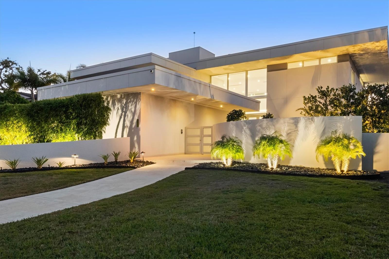 Step into an architectural masterpiece that exudes modern luxury and sophistication. Designed by renowned architect Carl Abbott, this residence captivates from the moment you arrive, with an expansive travertine walkway leading to a Zen garden. Glass double doors open to a bright, expansive great room, where a wall of windows and pocketing sliders frame unobstructed water views. White-oak engineered floors and a marble fireplace create a warm, refined backdrop, complemented by a handcrafted paper-mâché chandelier made by a German artist. The Valcucine® kitchen is a showpiece of innovation and craftsmanship, with custom cabinetry that folds away to reveal or conceal what’s inside. Granite countertops outline the perimeter, and a sliding countertop section hides the Miele® induction cooktop or sink when not in use. The island features a granite top with a wood edge for dining, complemented by a top-tier appliance suite including a Sub-Zero refrigerator, wine cooler, and beverage drawers, along with a Miele® dishwasher, convection microwave, dual wall ovens, and espresso machine. Every detail is considered, from hidden outlets and spice racks to a walk-in pantry with professional-grade organization. The primary suite occupies the second level, accessed by a sleek staircase with glass rails or the elevator. This loft-style retreat features engineered white oak floors, a generous seating area, and sliders opening to a private upper terrace. A sliding wood wall adds privacy while preserving natural light. The en-suite bath showcases floor-to-ceiling tile, a freestanding soaking tub, oversized Roman shower, and a lighted floating vanity with quartz countertops. Two expansive custom walk-in closets complete the suite. Three additional bedrooms each offer unique design touches. One, currently a media room, opens to a private terrace. Guest baths feature walk-in showers and custom vanities, while a dedicated fitness studio provides space for wellness and recreation. Outdoor living is equally inspired, with a travertine pool deck, covered and open seating areas, a boat dock with lift, and a heated pool and spa. Sunshades, an outdoor shower, and a spacious lawn complete the experience. The rooftop deck, accessible by elevator, serves as the ultimate entertaining space with panoramic views and a wet bar. This home is equipped with a three-stop hydraulic elevator, full smart home integration, triple-pane hurricane-rated windows and doors, a whole-house generator and water filtration system, central vacuum, architectural linear HVAC grilles, and in-floor outlets. Originally completed in 2002, the residence was completely rebuilt from the concrete pad and bearing walls in 2016, including all electrical, plumbing, HVAC, roofing, rooftop deck, hurricane glass, appliances, fixtures, flooring, pool and spa systems, and smart technology. San Remo Estates occupies a premier position at the heart of Sarasota, tucked just before the north bridge to Siesta Key. This coveted waterfront enclave offers the perfect balance of privacy and convenience, placing residents minutes from the iconic white-sand beaches and village of Siesta Key, the vibrant shops and restaurants of Southside Village, and the cultural energy of Downtown Sarasota.