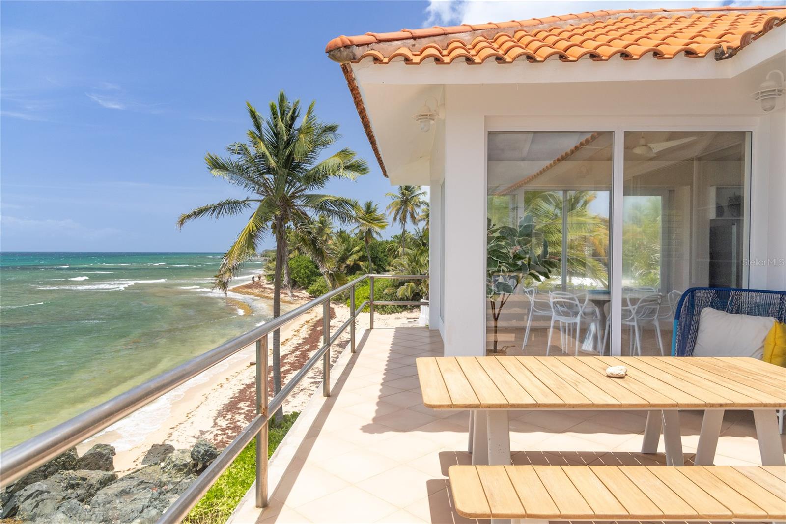 Las Piedras is an exceptional oceanfront estate offering sweeping panoramic views and a profound connection to its natural surroundings. Perched above the crystalline waters of Vieques’ coveted north shore, the residence commands a dramatic 180-degree vista of the Caribbean Sea—from the coral-fringed shoreline below to the distant silhouettes of Culebra, St. Thomas, and St. John along the horizon. To the west, the mountains of mainland Puerto Rico rise in the distance, completing a truly immersive island panorama.

A private palm-lined drive, framed by tropical foliage, leads to the home’s striking entrance. The architecture blends clean contemporary lines with subtle Spanish Colonial influences, highlighted by a terracotta-tiled hipped roof. Thoughtfully constructed across three levels, the residence offers four bedrooms, two and a half baths, and a seamless integration of indoor and outdoor living spaces designed to embrace the surrounding seascape.

The upper level serves as the home’s architectural and social centerpiece. Vaulted ceilings crown an open-concept kitchen, dining, and living area, where floor-to-ceiling glass captures uninterrupted ocean views from nearly every vantage point. The living space extends to a generous ocean-facing terrace—an ideal setting for sunset dining, lounging, and entertaining. A powder room and adjacent flex space, currently arranged as a sleeping area, offer versatility with potential for conversion to an additional full bath.

A sculptural central staircase, artfully integrated into natural boulders that form part of the home’s foundation, anchors the structure with organic elegance. The second level hosts the primary sleeping quarters, including two bedrooms—both with ocean views. The principal suite features a refined ensuite bath with a polished cement shower and integrated sink. A secondary sitting room with a concealed Murphy bed opens onto a balcony overlooking the sea and connects directly to the pool terrace. An additional full bath on this level includes an oversized built-in tiled soaking tub.

On the ground floor, two additional well-proportioned bedrooms—each with ocean views—offer privacy and comfort, along with a shared sitting area and reading nook. A full bath with polished cement finishes, as well as a spacious laundry and storage room, complete the level. All four bedrooms enjoy direct ocean views and are fully air-conditioned, while the remainder of the home is designed to maximize natural cross-ventilation and cooling sea breezes.

Outdoors, the property is both private and commanding, with direct access to the tranquil sands of La Chata Beach. Native palms and low-maintenance tropical landscaping frame a walking path that encircles the residence, providing effortless access to multiple vantage points. A gated entrance opens to a private parking area accommodating two vehicles, while a discreetly positioned utility and pump room is tucked beneath the pool deck.

Equally suited as a private coastal sanctuary or a high-performing investment asset, Las Piedras is currently operated as a successful luxury vacation rental with a proven income history. Rarely does a property combine architectural presence, privacy, and panoramic ocean views from every bedroom in such a compelling and turnkey offering.