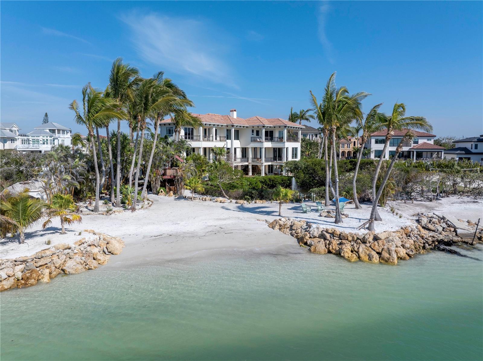 * Pending. Accepting backup offers.* Nestled along the pristine northern shores of Siesta Key, this magnificent three-story waterfront retreat redefines coastal luxury and exclusivity. The home features 10,600 sq ft under roof with approximately 5,500sq ft under air. This exceptional home is crafted for grand entertaining and effortless relaxation. While Siesta Beach and Village are just minutes away by golf cart, the gated personal estate ensures total privacy, creating a secluded paradise where the rhythm of the waves and the beauty of the Gulf serve as the ultimate backdrop.

As you approach, a sprawling driveway and state-of-the-art security gates provide both exclusivity and convenience, granting access to a four-car garage, perfect for luxury vehicles, watercraft, or additional storage. Stepping inside, you’re greeted by a grand entrance with a 34-foot-high foyer. Up the stairs you will find walls of glass showcasing unobstructed Gulf panoramas. Expansive retractable glass doors erase the line between indoors and out, immersing you in the stunning coastal setting from the moment you arrive.
Descending to the main living level, a chef’s dream kitchen awaits, masterfully designed with thick quartz countertops, a spacious center island, and a custom eight-seat breakfast bar. Flowing seamlessly into sun-drenched living and dining areas, this space is enhanced by towering 12-foot ceilings, creating an atmosphere of grandeur and warmth. A hidden bonus room unveils a fully equipped outdoor kitchen and entertainment lounge, offering a seamless transition to alfresco dining and unforgettable gatherings under the stars.

The upper levels of the home are dedicated to rest and rejuvenation, with four private bedroom suites, each offering breathtaking Gulf views, intimate balconies, and spa-inspired en-suite baths. The primary suite, a haven of tranquility, boasts 270-degree water views, expansive lounging terraces, and a marble-clad spa bath, designed to capture the essence of relaxation and indulgence.

Beyond the home’s elegant interiors lies a spectacular tropical oasis. Designed by the renowned Lucas Lagoons, the lagoon-style pool and spa feature a cascading waterfall, offering the ultimate retreat for relaxation. A meandering stone pathway winds through the gorgeous landscape, passing a serene saltwater tidal pond, leading to a two-story Tiki retreat, an idyllic setting for sunset cocktails and ocean breezes. At the edge of the property, a Gulf-front fire pit, nestled into the immaculate white sands, invites you to unwind as the sky transforms into a breathtaking masterpiece of colors.

Whether envisioned as a luxurious primary residence or an exceptional coastal retreat, this one-of-a-kind Gulf-front estate offers an unparalleled blend of seclusion, sophistication, and effortless luxury. With unrivaled beach frontage and panoramic water views, this property is more than just a home—it is a rare opportunity to own a true piece of paradise on one of the most coveted stretches of Siesta Key. This listing does not include the lot at 0 Solymar Dr. MLS number (A4642147). Creative Seller Financing Available!