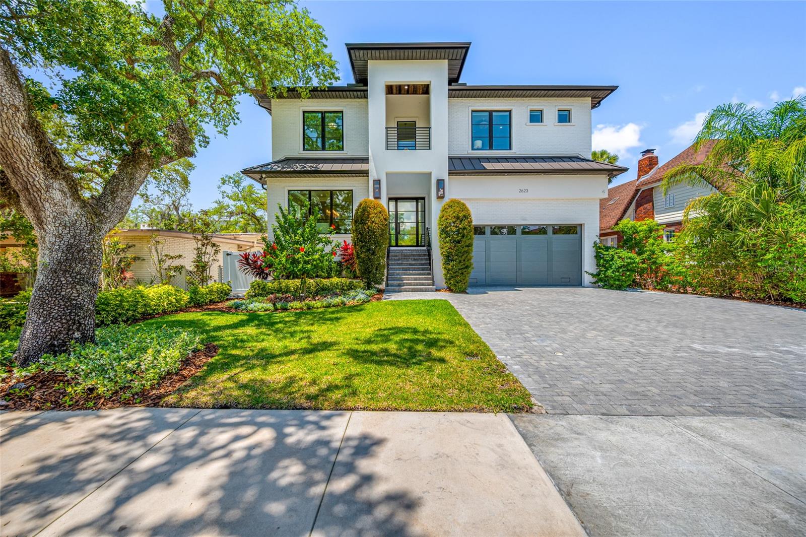 Poised within the coveted Sunset Park neighborhood and in the highly desirable Plant High School District, this Baywalk Custom Homes residence built in 2021 is a masterclass in modern luxury—where architectural elegance, curated materials, and fully integrated smart home technology converge. Set on an impressive 157-foot deep homesite and elevated above the flood zone, the home offers 5 bedrooms, 5.5 baths, a private study, bonus retreat, and nearly 5,000 square feet of refined living. A striking façade introduces the home with a custom iron entry door framed by glowing gas lanterns and clean architectural lines. Inside, a dramatic foyer unfolds into a light-filled interior defined by wide-plank oak floors, crisp detailing, and soaring ceilings with subtle tray accents. The formal dining space feels both elevated and inviting, while a discreetly placed powder room reflects thoughtful design. The main living area is anchored by a sleek Monessen Artisan fireplace and enhanced by exposed beam detail. At the center, the kitchen is sculptural and modern. A waterfall-edge marble island serves as both focal point and gathering space, complemented by a full Thermador suite including a 48-inch refrigerator/freezer, six-burner gas range with griddle, double ovens, and pot filler. A butler’s pantry with beverage drawers, wine refrigeration, and custom cabinetry supports effortless hosting, while an oversized walk-in pantry with built-ins and a dedicated coffee bar elevates everyday living.
Designed with lifestyle in mind, the home features a state-of-the-art smart system controlling lighting, climate, security, and audio throughout. A dedicated theatre-style media experience with immersive surround sound, whole-home audio distribution, and integrated outdoor speakers—including poolside sound—create a cohesive, elevated environment tailored for both relaxation and entertaining. A main-level guest suite offers privacy and comfort, while the bonus room is complete with a designer dry bar, dual beverage refrigeration, ambient lighting, and motorized Hunter Douglas Powerview blackout shades—ideal for game days or evening gatherings. Upstairs, a tranquil loft connects to a private study enclosed by French doors—perfectly suited for work or quiet reflection. The primary suite is a serene escape, defined by clean lines. Motorized shades and integrated audio enhance comfort, while the spa-like bath and custom-designed dressing room has center island and direct access to the laundry suite. Each additional bedroom is generously proportioned and appointed with its own en-suite bath, ensuring both comfort and privacy. Dual-level travertine terraces frame a heated, fully automated saltwater pool and spa, complete with sun shelf, spillover feature, and tranquil water element. The summer kitchen is equipped with a 32-inch gas grill, professional hood, beverage refrigeration, prep sink, and tongue-and-groove ceiling with integrated audio. Lush landscaping and a private tidal canal backdrop provide a sense of calm seclusion. A 3 car tandem garage with elevated storage, a thoughtfully designed mudroom, and exceptional craftsmanship throughout complete the residence. This is a home where modern elegance meets intelligent design—crafted for those who value precision, beauty, and a fully connected living experience in one of Tampa’s most sought-after neighborhoods.