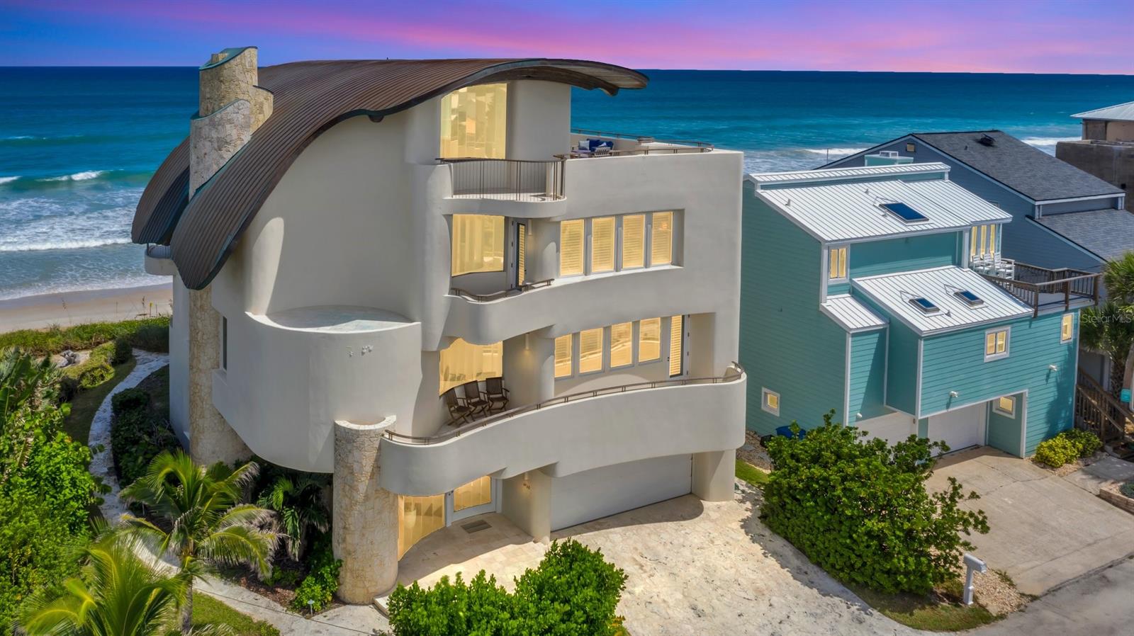 This stunning oceanfront property in NSB offers an unparalleled escape with breathtaking views of both the ocean and the Intracoastal Waterway. The home itself is a masterpiece of architecture, perched on a promontory above the expansive beach and enchanting dunes. It stands as one of the most distinguished waterfront residences in Central Florida, seamlessly blending ethereal charm with modern amenities.
Inspired by the natural beauty of the oceanfront location, the design captures the essence of the waves and the ocean's power. The structure's exotic shape and poetic details, complemented by imaginative amenities, make it truly exceptional. Features include a luxurious master suite, wet bar, theater room, two keystone fireplaces, and a fully equipped professional chef's kitchen with custom imported cabinetry from England and top-tier stainless-steel appliances (Sub-Zero, Miele, Thermador).
The interior is anchored by a dramatic four-story travertine spiral staircase, leading to overlook lofts on all levels and a roof terrace with panoramic views of the ocean to the east and the river to the west. The curving roof structure, constructed with laminated beams, timber wood decking, and copper cladding, adds to the home's unique appeal. Teak and stainless steel are used for exterior railings and cabinetry. The design seamlessly connects the interior and exterior with indigenous Florida Keystone, hand-textured plaster, and expansive segmented butt-joined glass.
This extraordinary beachfront residence combines the essence of California's Gold Coast, Southampton, NY, and Palm Beach. If situated in any of those locales, its market value would be five times that of NSB. This charming beach town offers local culture, year-round beach activities, festivals, parades, excellent dining, boutique shopping, art, and a beautiful sandy shoreline. ;Water: City
